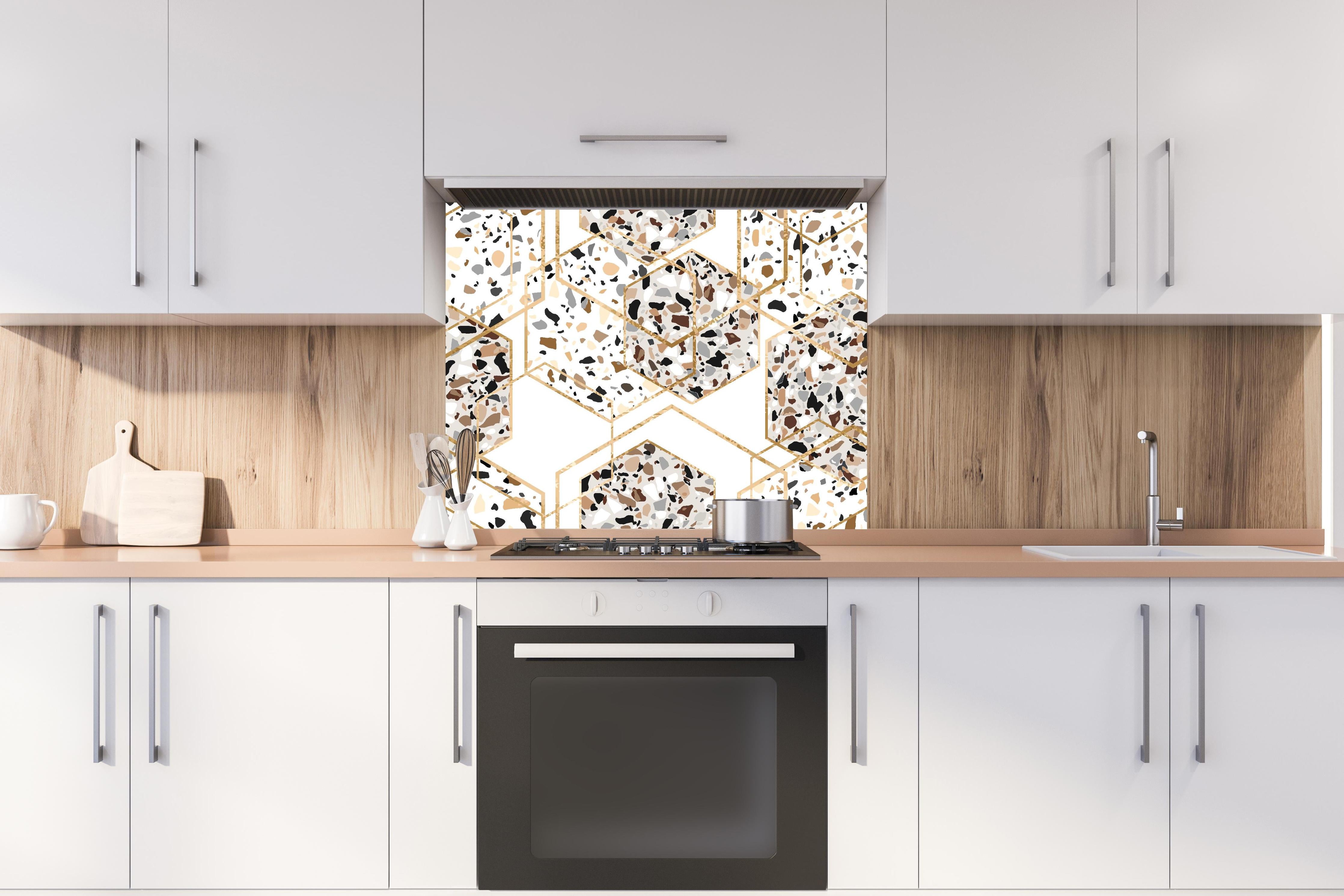 Spritzschutz - Trendiges Terrazzo-Muster mit Goldakzenten hinter einem Cerankochfeld zwischen Holz-Kochutensilien