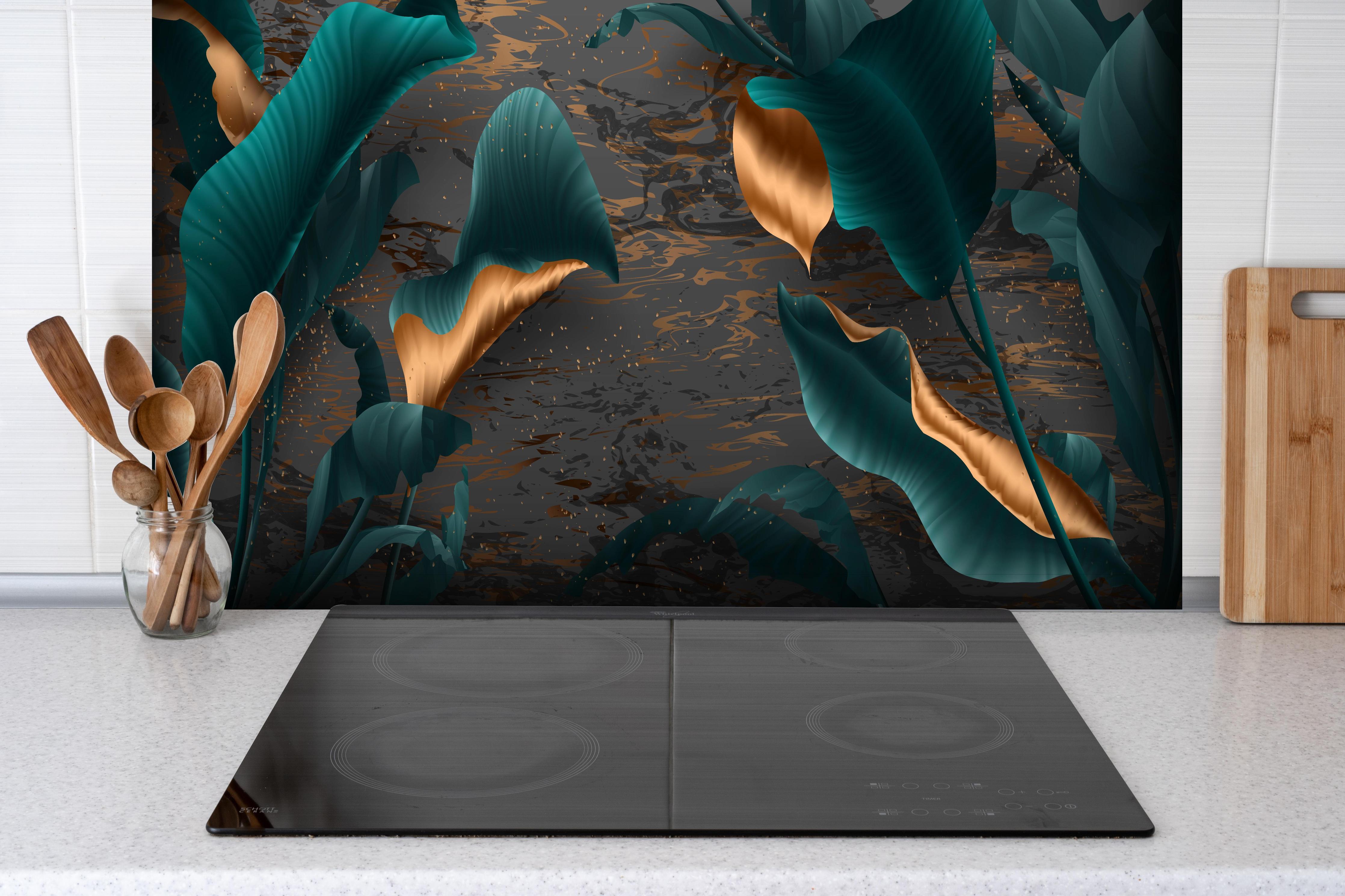 Spritzschutz - Tropische Blätter mit goldener Marmorierung hinter einem Cerankochfeld zwischen Holz-Kochutensilien