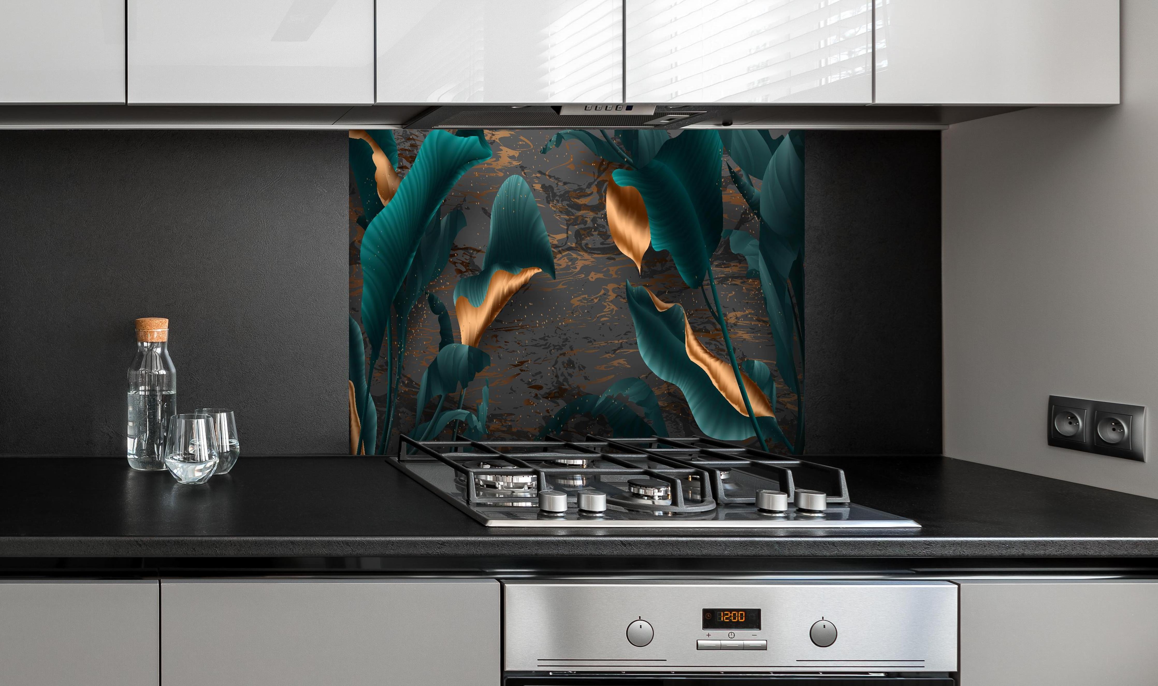 Spritzschutz - Tropische Blätter mit goldener Marmorierung hinter einem Cerankochfeld zwischen Holz-Kochutensilien