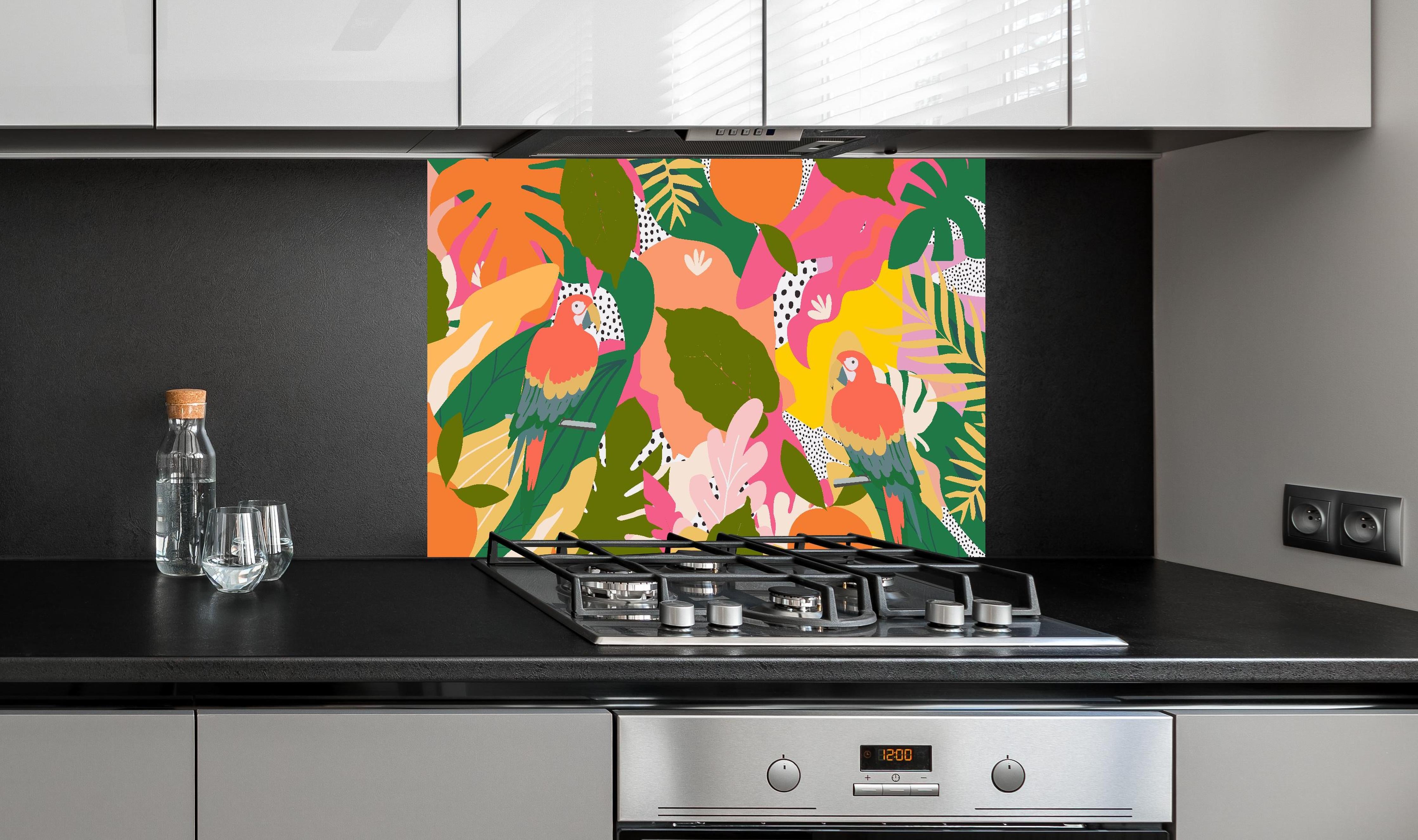 Spritzschutz - Tropischer Dschungel mit bunten Papageien hinter einem Cerankochfeld zwischen Holz-Kochutensilien