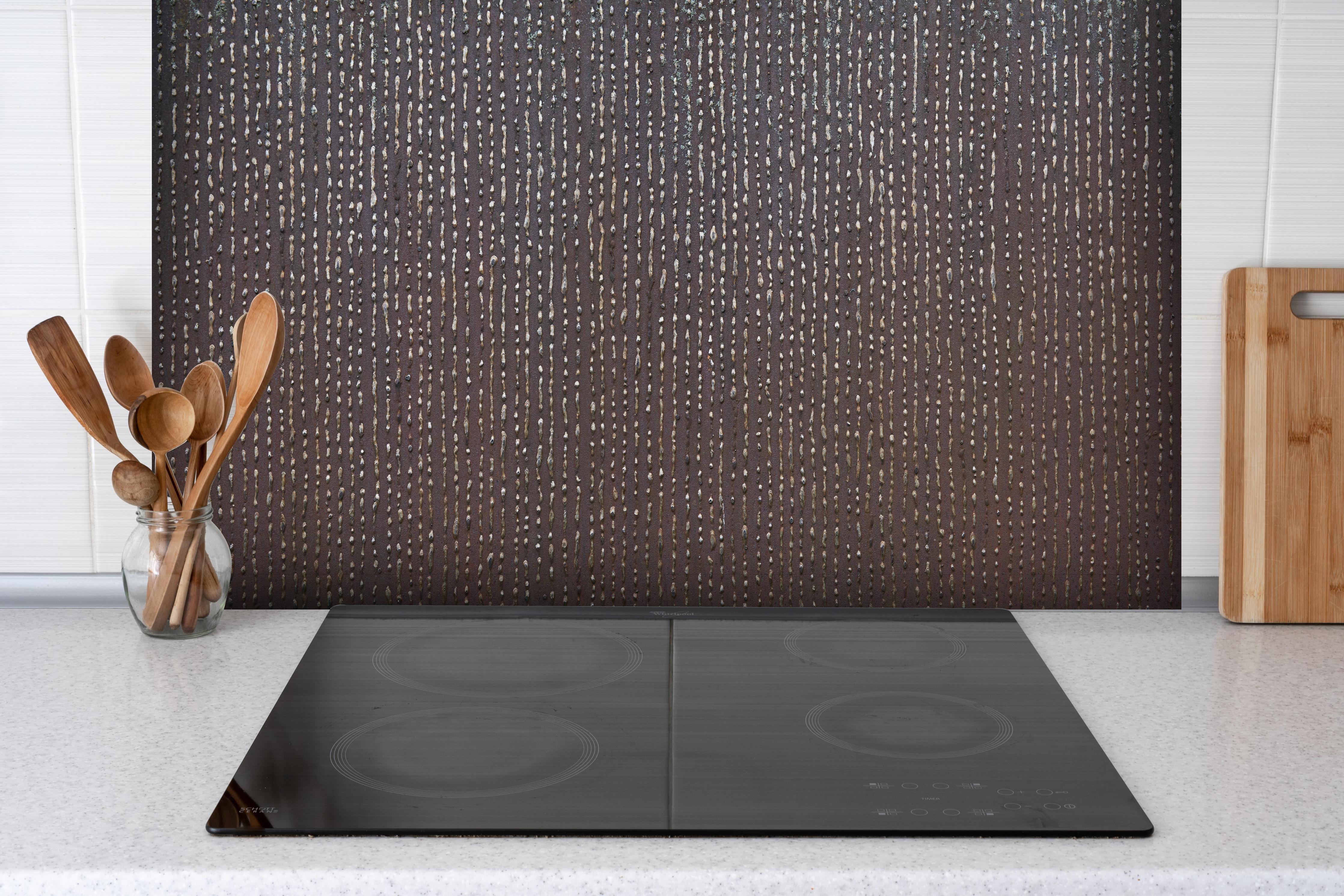 Spritzschutz - Ungewöhnliche Tropfenstruktur hinter einem Cerankochfeld zwischen Holz-Kochutensilien