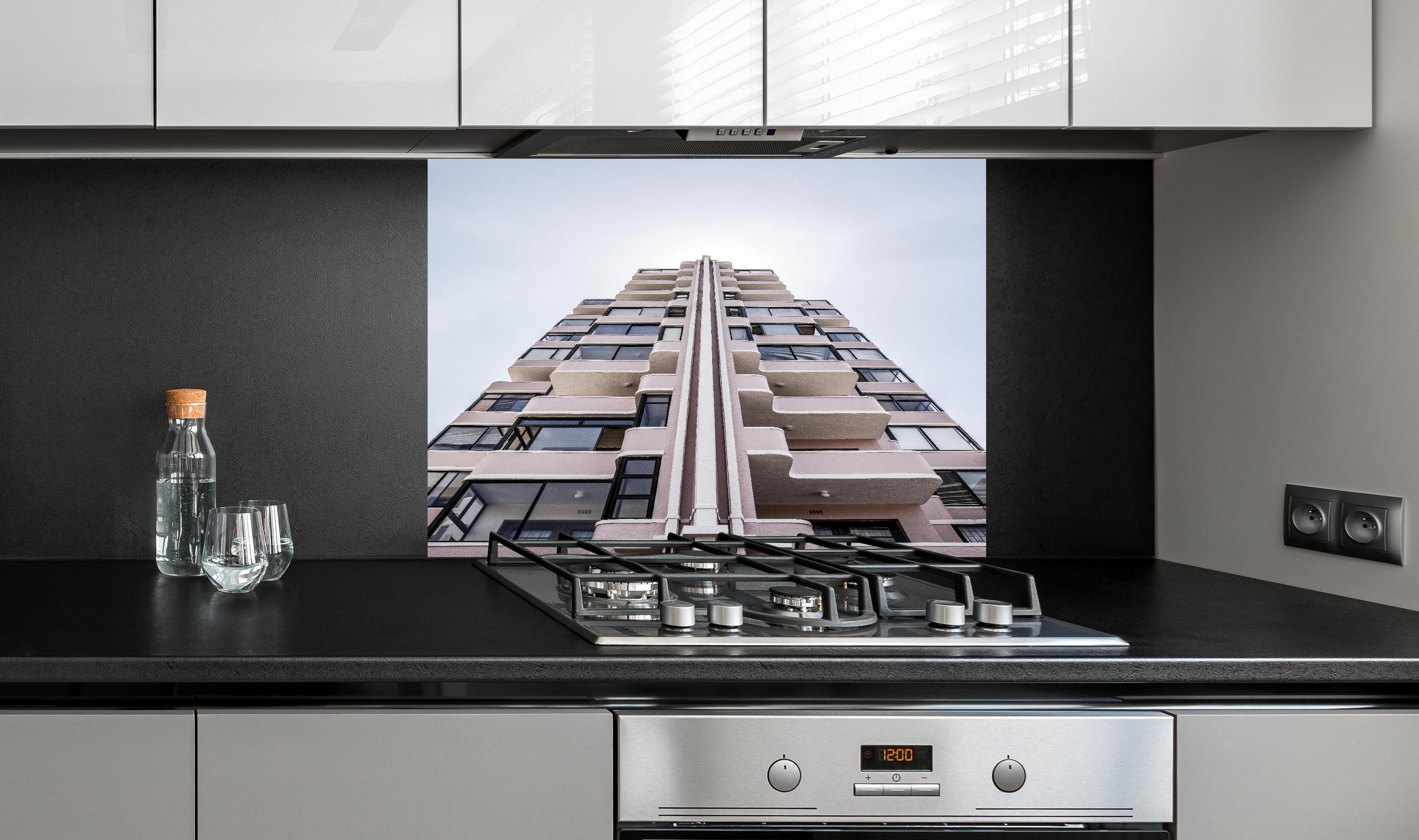 Spritzschutz - Urbanes Hochhaus mit grau-beigen Akzenten hinter einem Cerankochfeld zwischen Holz-Kochutensilien