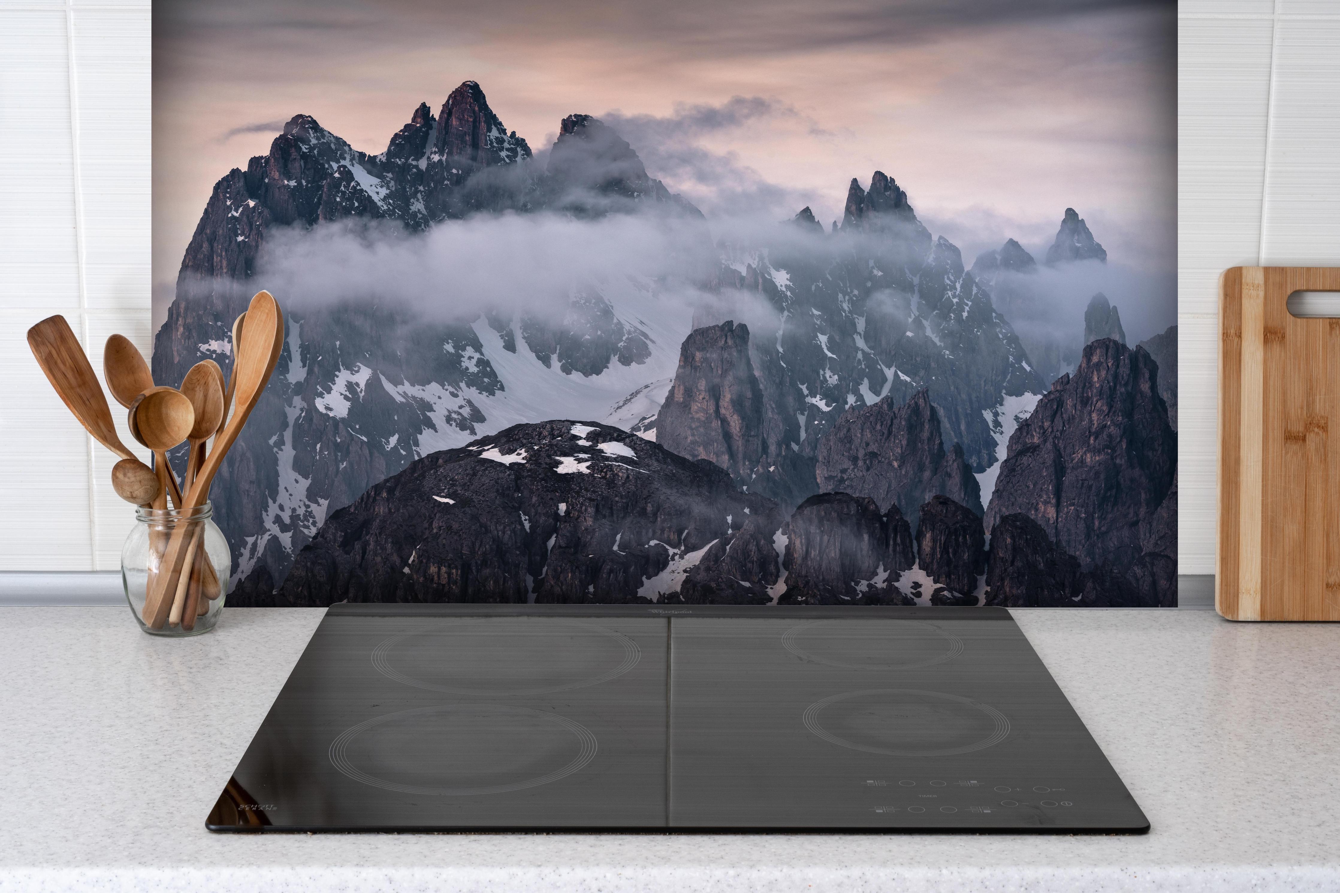 Spritzschutz - Verschneite Berggipfel bei Abenddämmerung hinter einem Cerankochfeld zwischen Holz-Kochutensilien