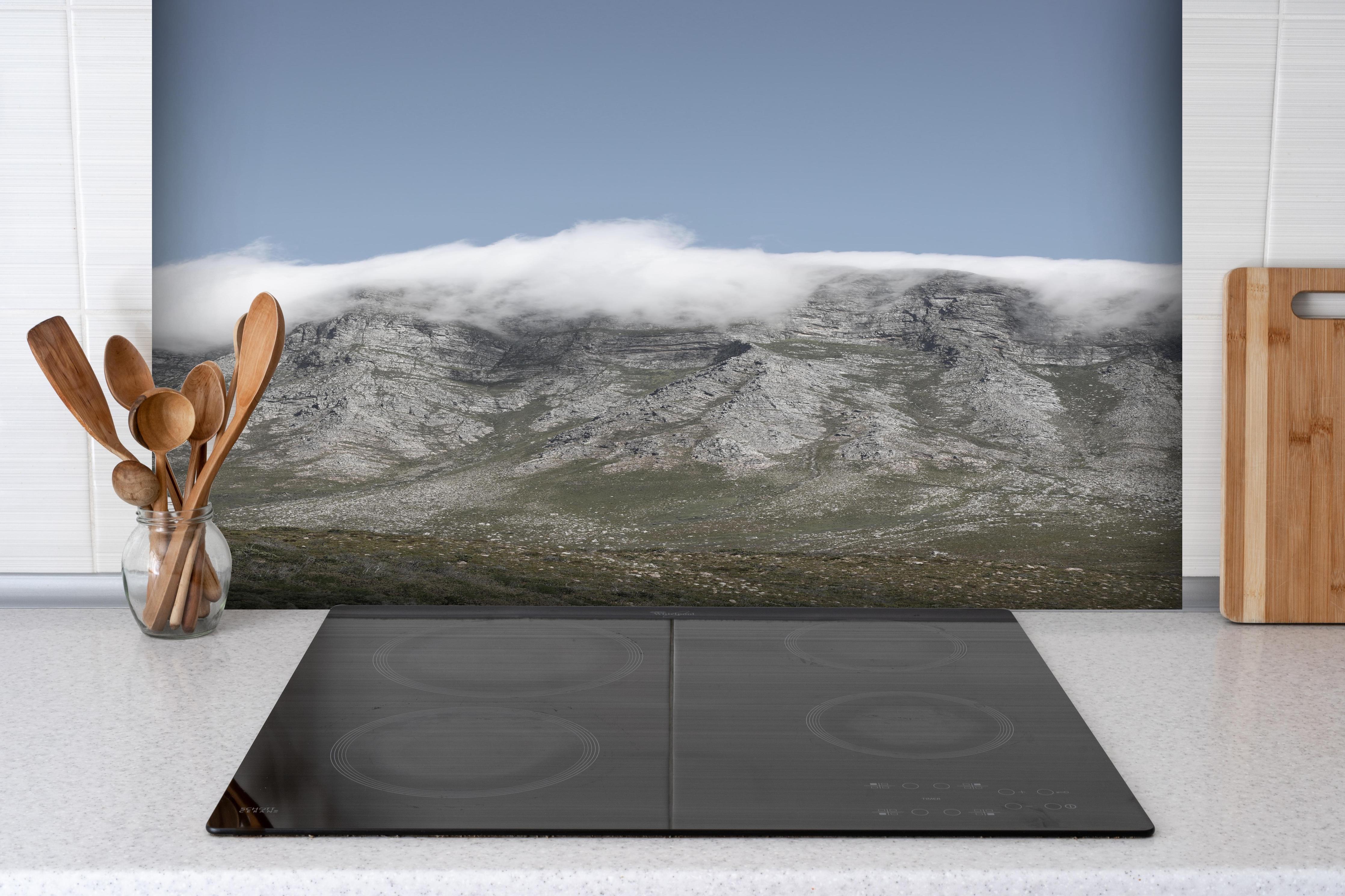 Spritzschutz - Verträumte Berglandschaft mit Wolkenverhang hinter einem Cerankochfeld zwischen Holz-Kochutensilien