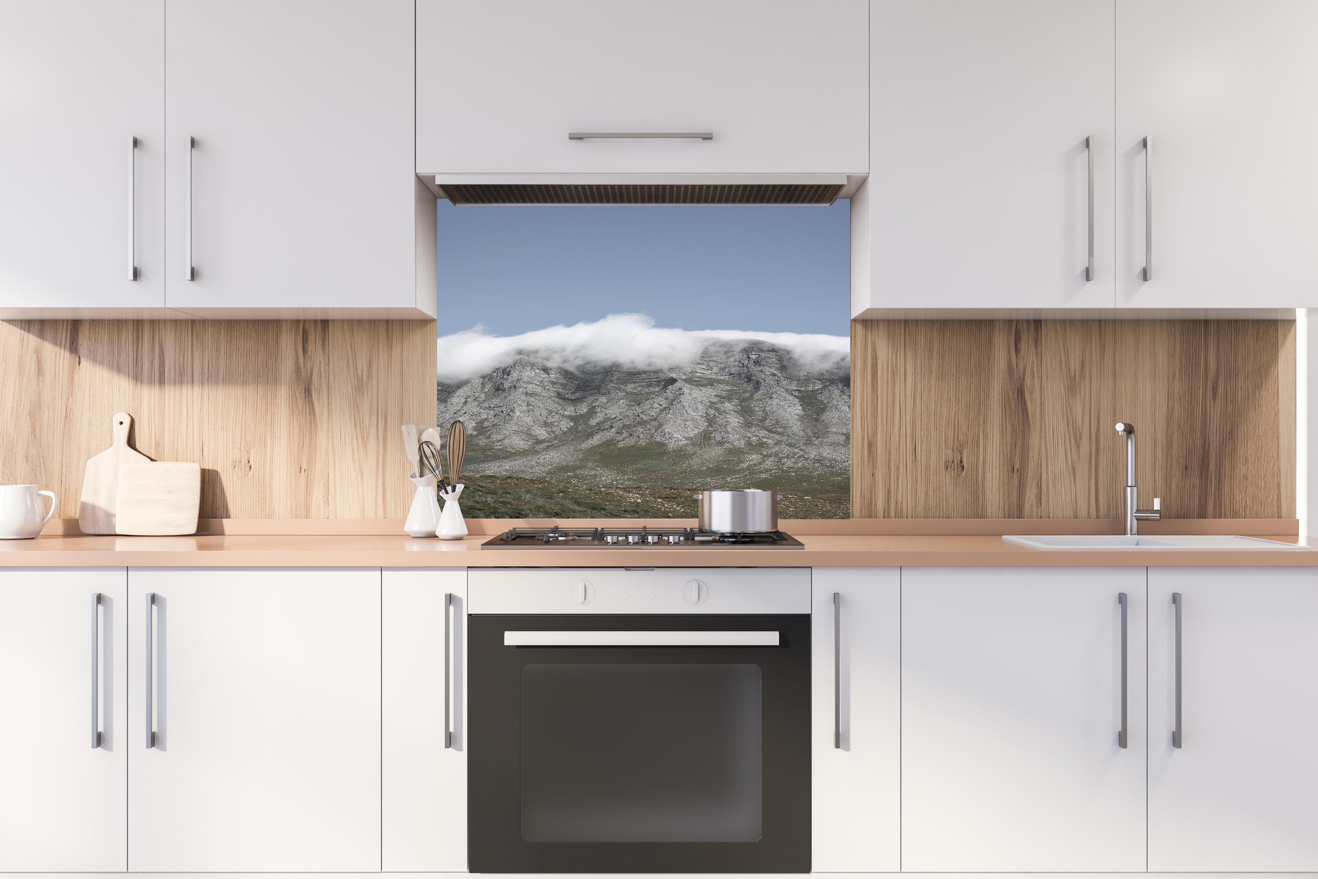 Spritzschutz - Verträumte Berglandschaft mit Wolkenverhang hinter einem Cerankochfeld zwischen Holz-Kochutensilien