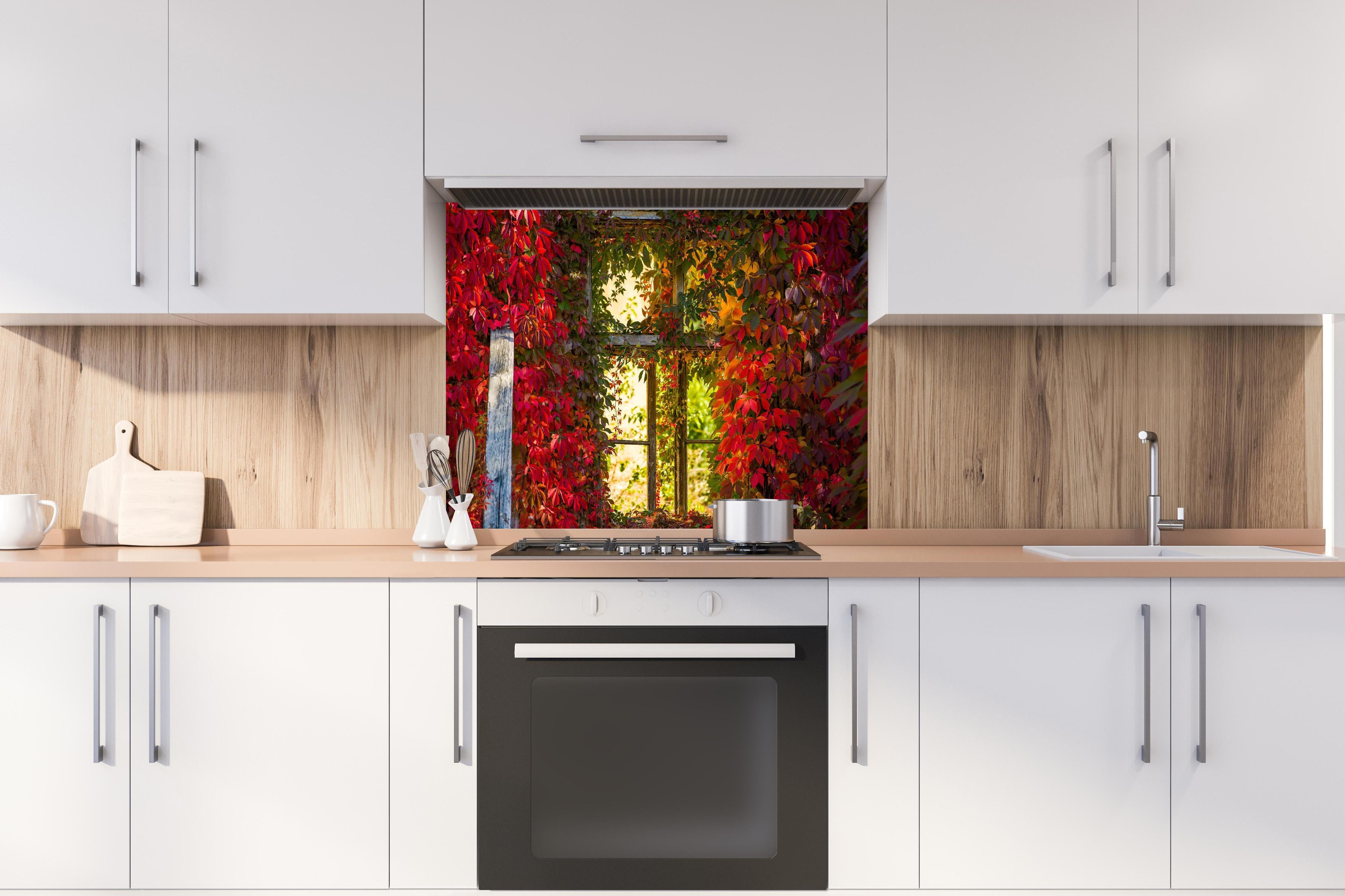 Spritzschutz - Verwachsenes Fenster mit roten Blättern hinter einem Cerankochfeld zwischen Holz-Kochutensilien