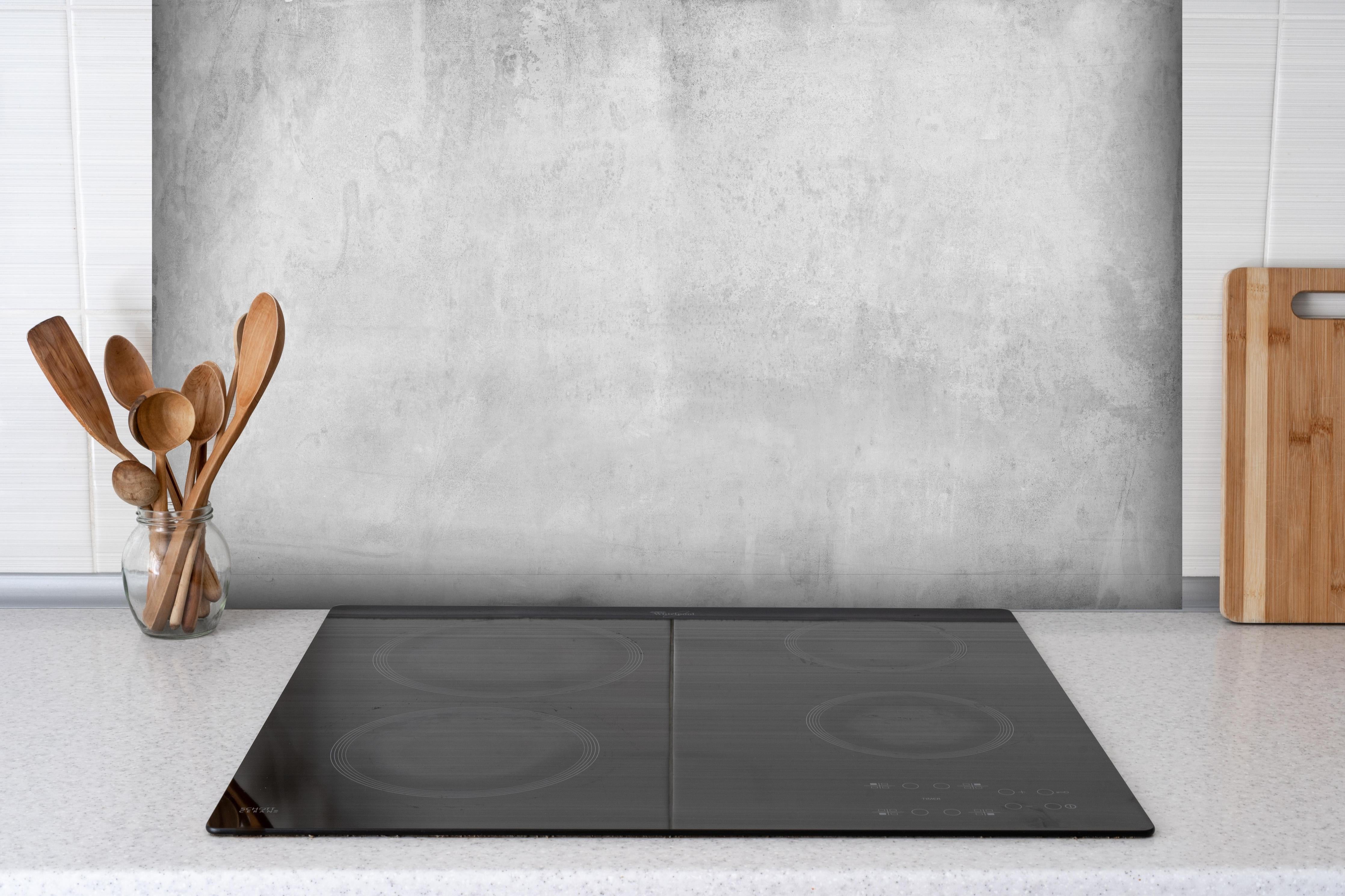 Spritzschutz - Verwitterte graue Zementwand hinter einem Cerankochfeld zwischen Holz-Kochutensilien