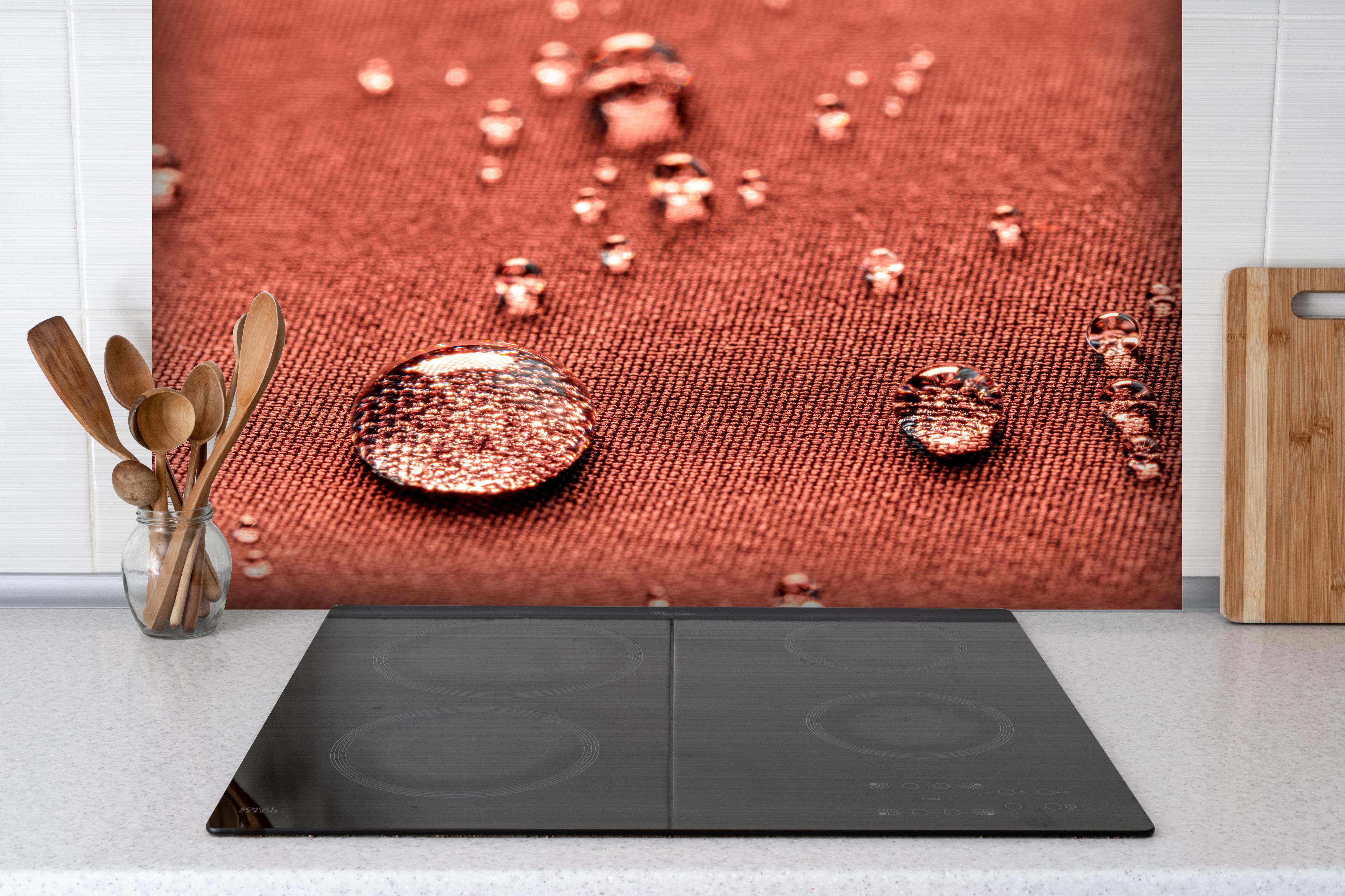 Spritzschutz - Wassertropfen auf rotem Stoff hinter einem Cerankochfeld zwischen Holz-Kochutensilien