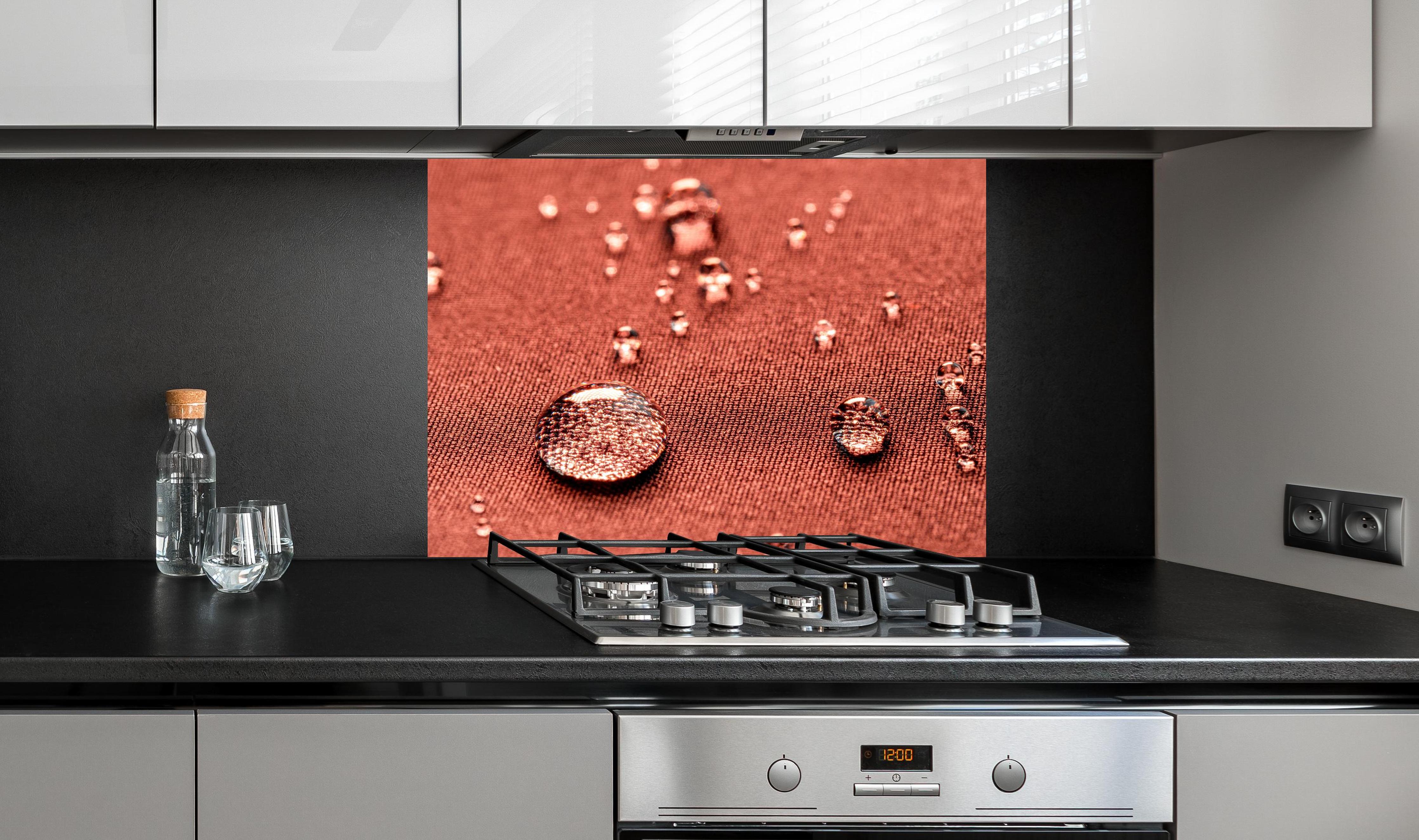 Spritzschutz - Wassertropfen auf rotem Stoff hinter einem Cerankochfeld zwischen Holz-Kochutensilien