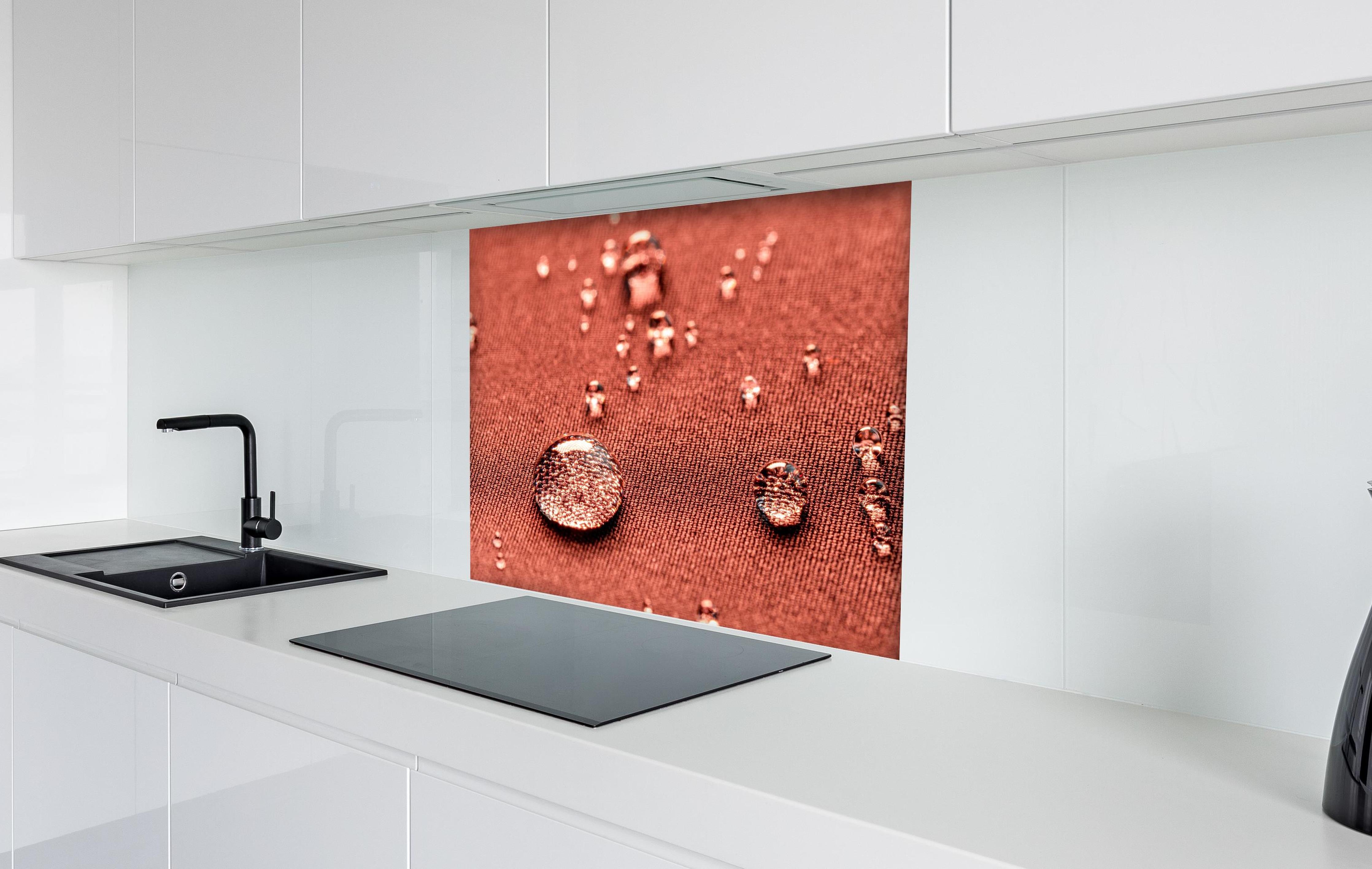 Spritzschutz - Wassertropfen auf rotem Stoff hinter einem Cerankochfeld zwischen Holz-Kochutensilien