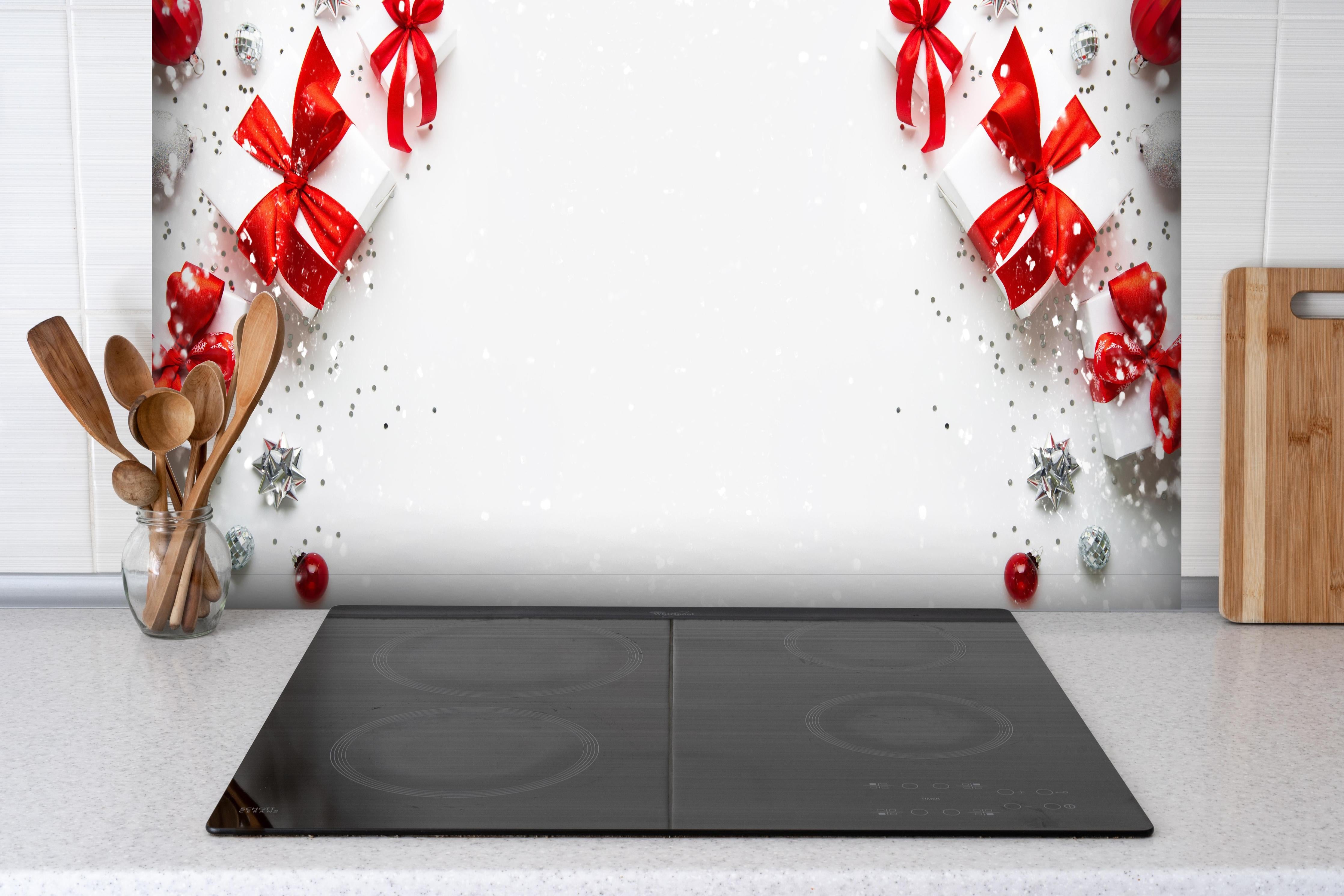 Spritzschutz - Weihnachtliche Geschenke mit Roter Schleife hinter einem Cerankochfeld zwischen Holz-Kochutensilien