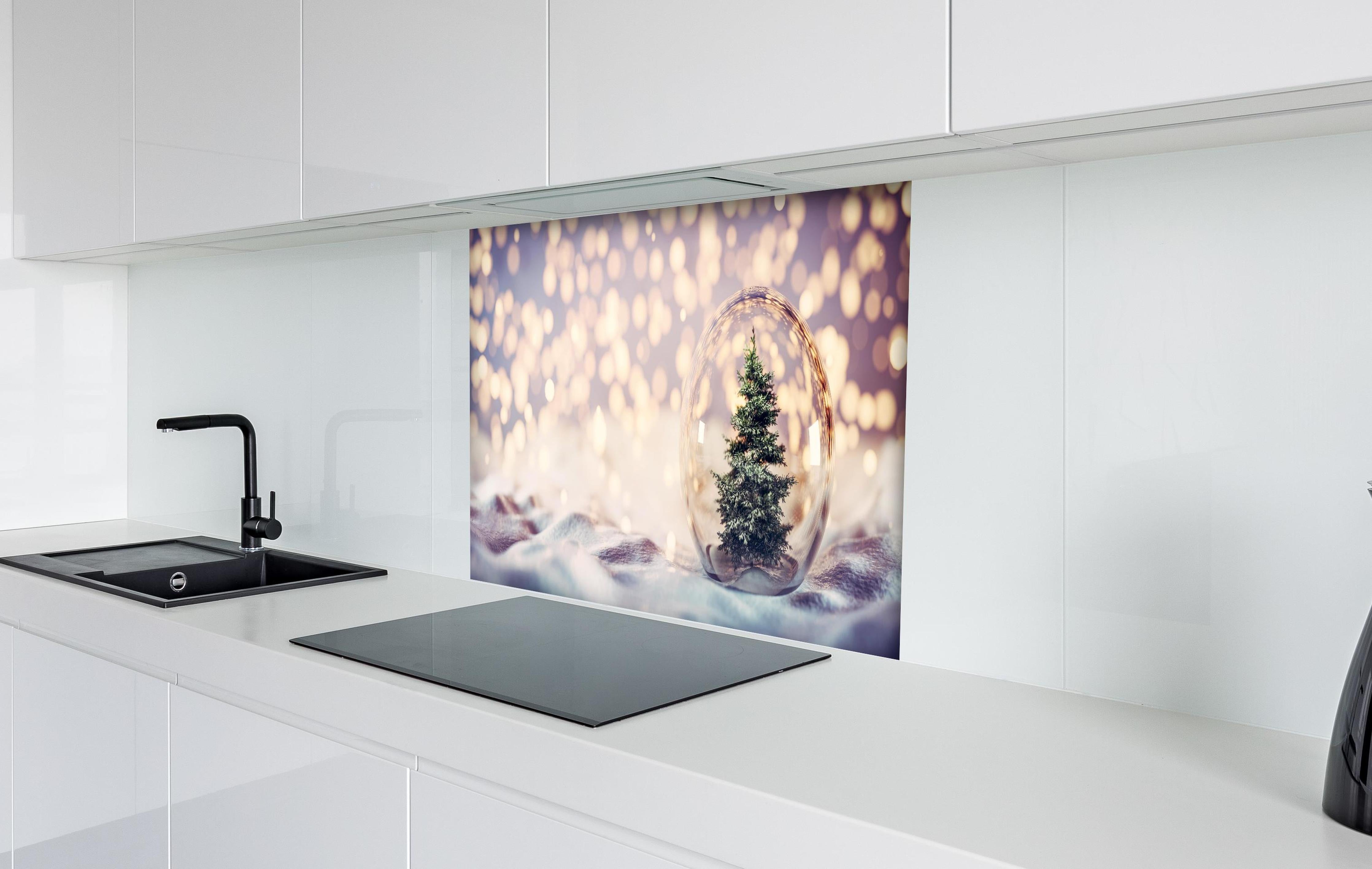 Spritzschutz - Weihnachtsbaum in einer Glaskugel hinter einem Cerankochfeld zwischen Holz-Kochutensilien