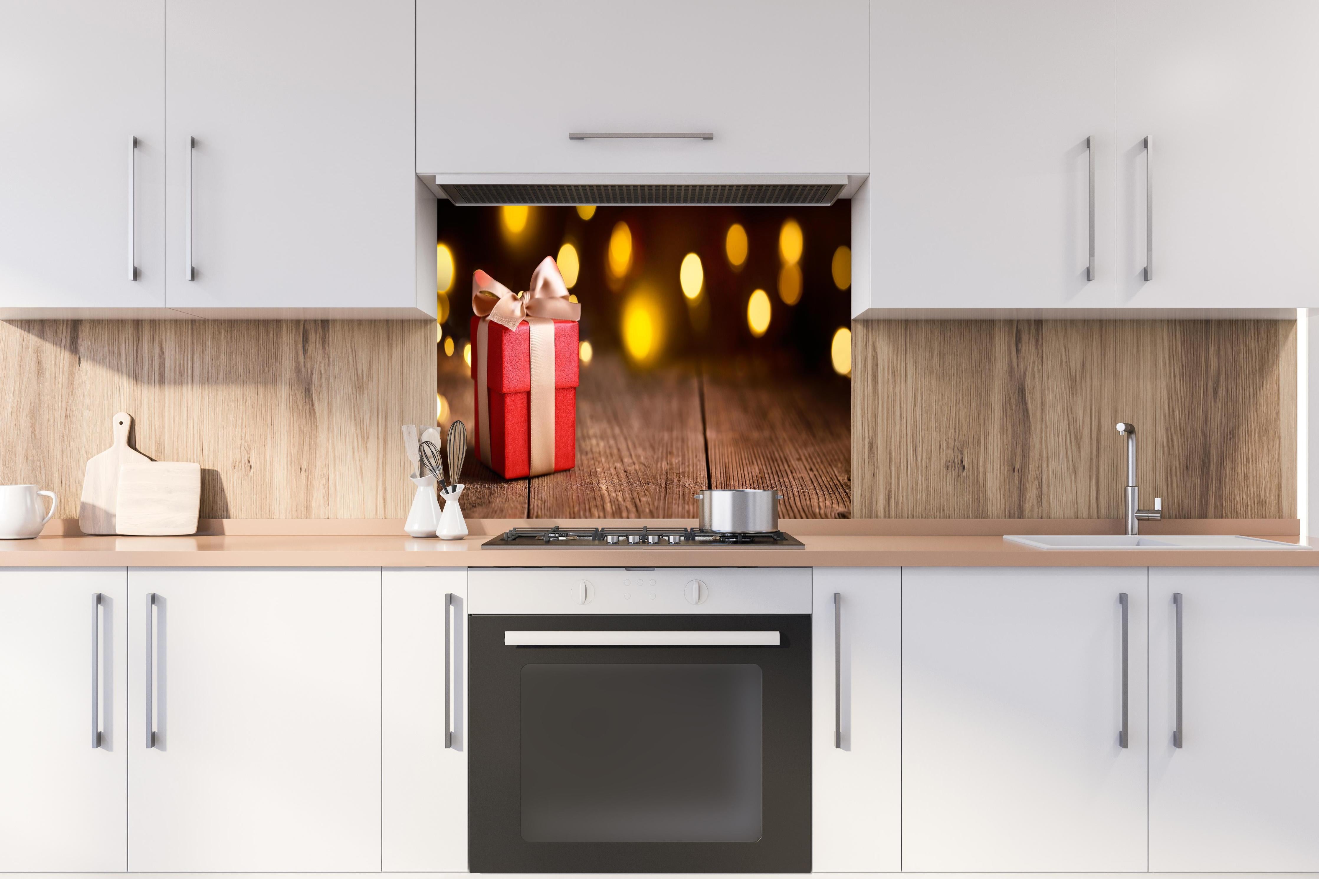 Spritzschutz - Weihnachtsgeschenk auf festlichem Hintergrund hinter einem Cerankochfeld zwischen Holz-Kochutensilien