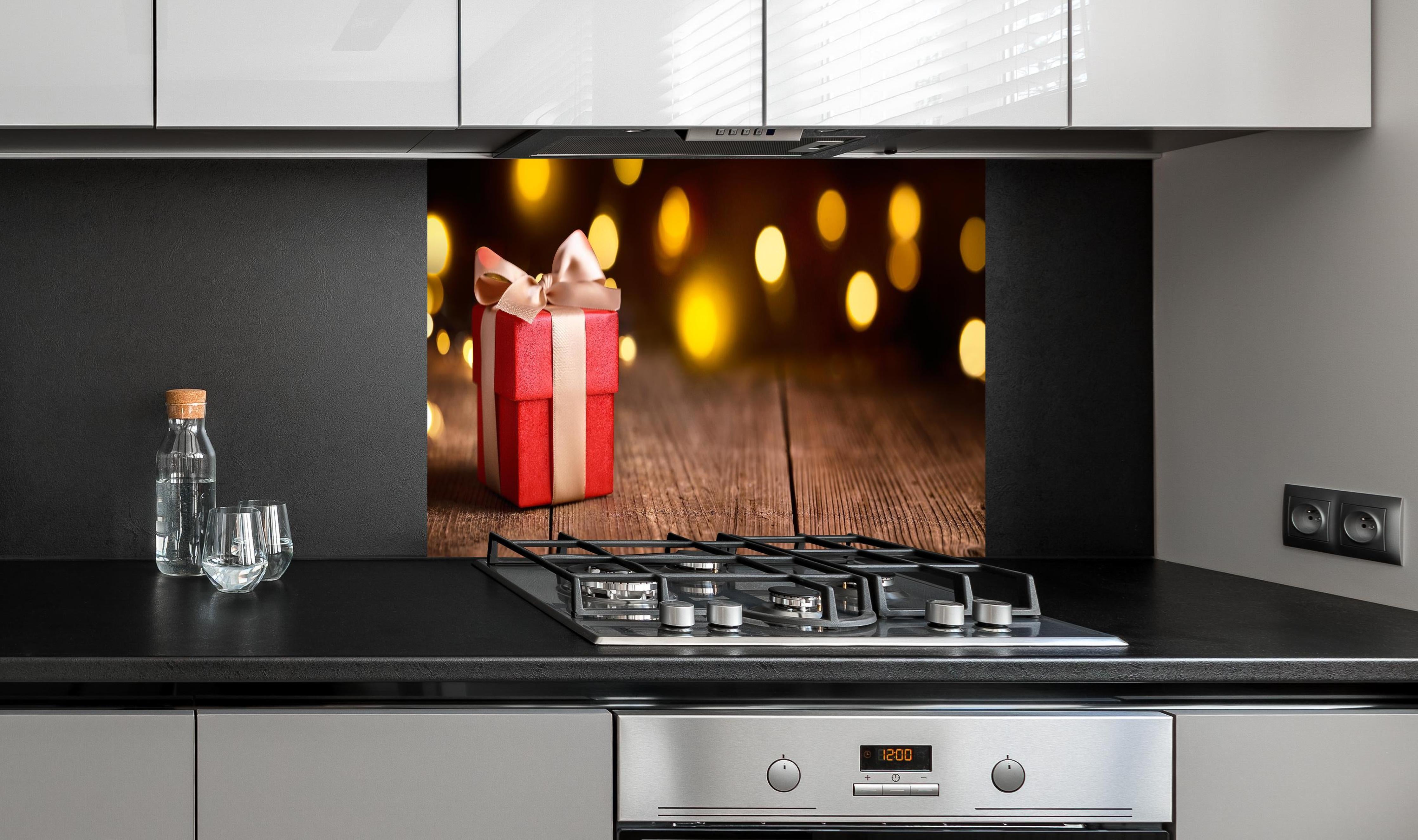 Spritzschutz - Weihnachtsgeschenk auf festlichem Hintergrund hinter einem Cerankochfeld zwischen Holz-Kochutensilien