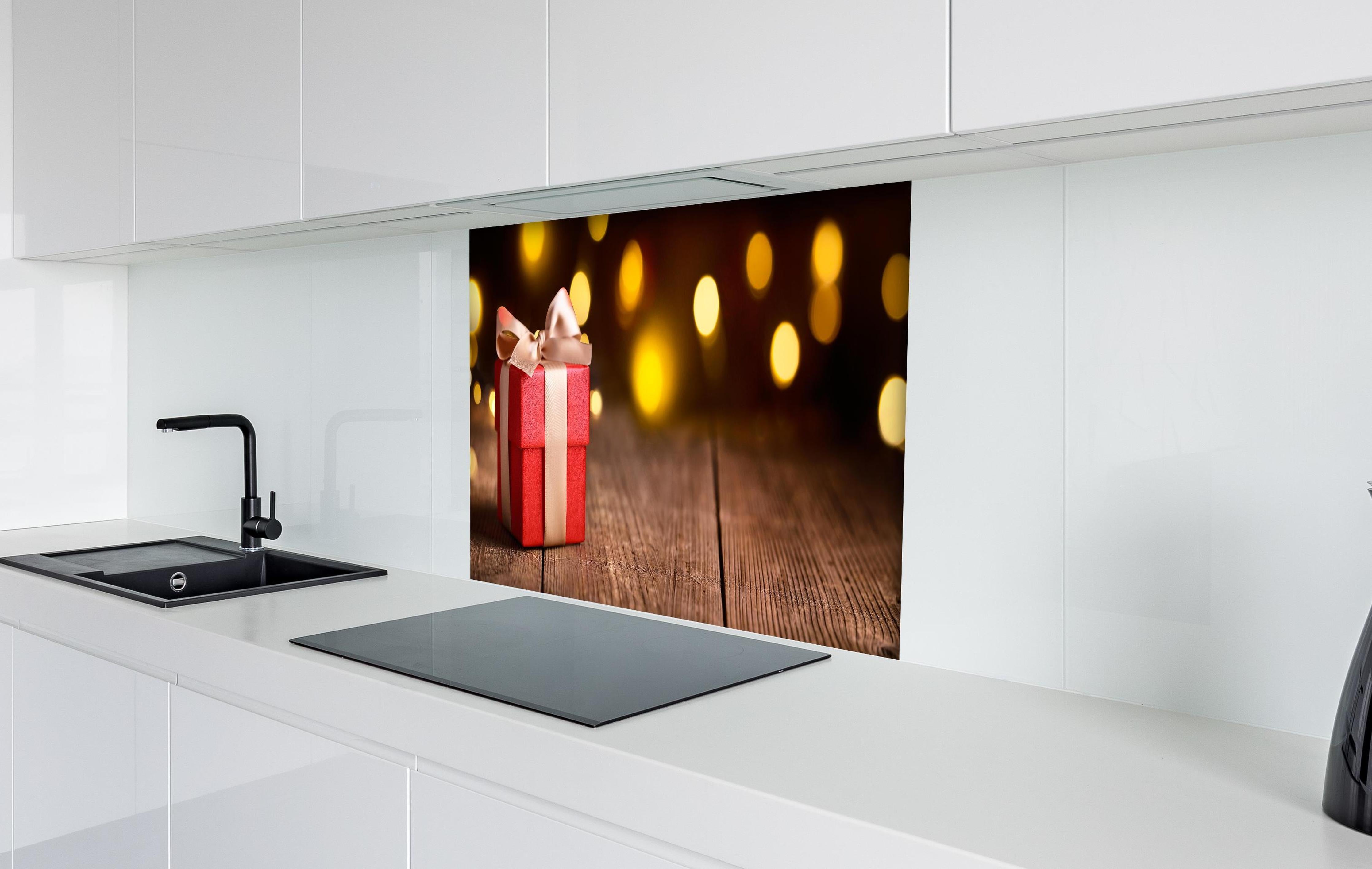 Spritzschutz - Weihnachtsgeschenk auf festlichem Hintergrund hinter einem Cerankochfeld zwischen Holz-Kochutensilien