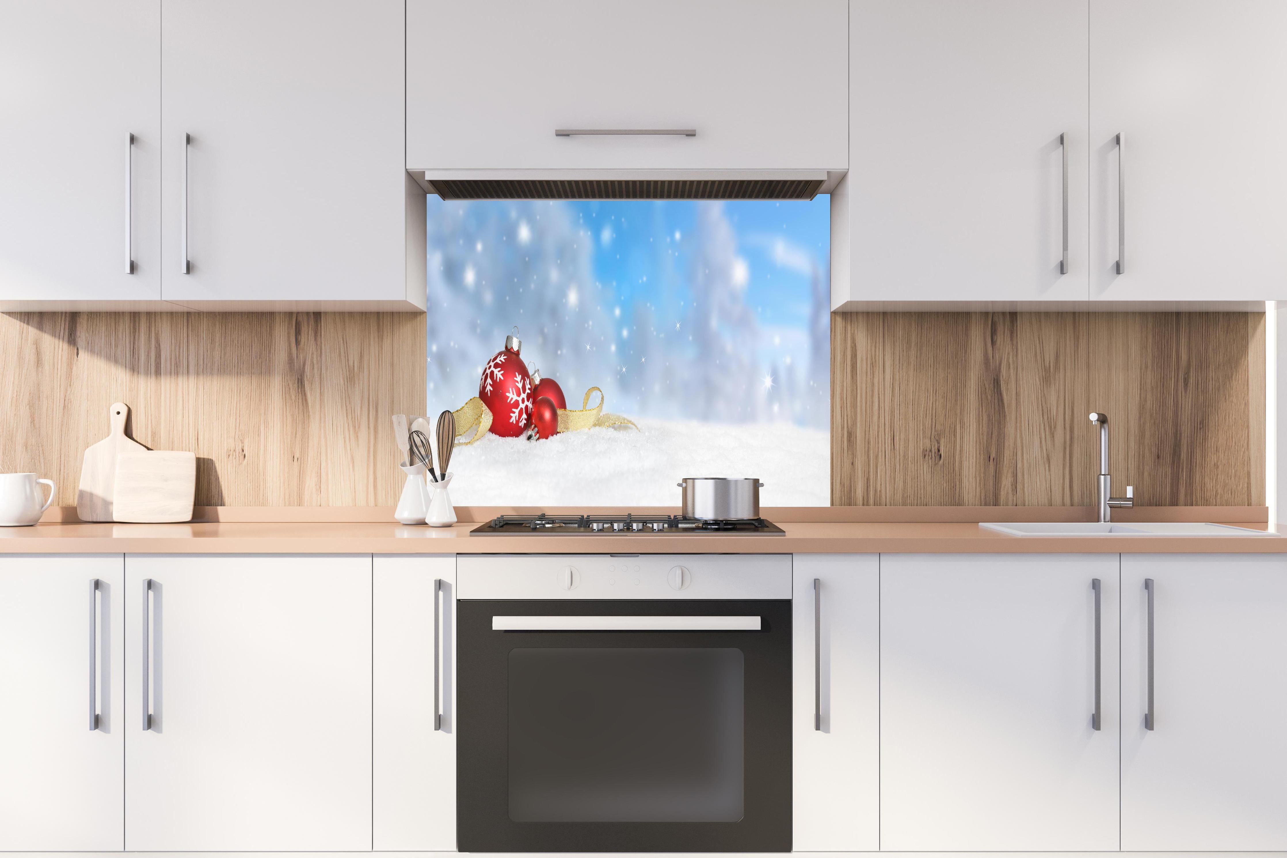 Spritzschutz - Weihnachtskugeln im Schnee hinter einem Cerankochfeld zwischen Holz-Kochutensilien