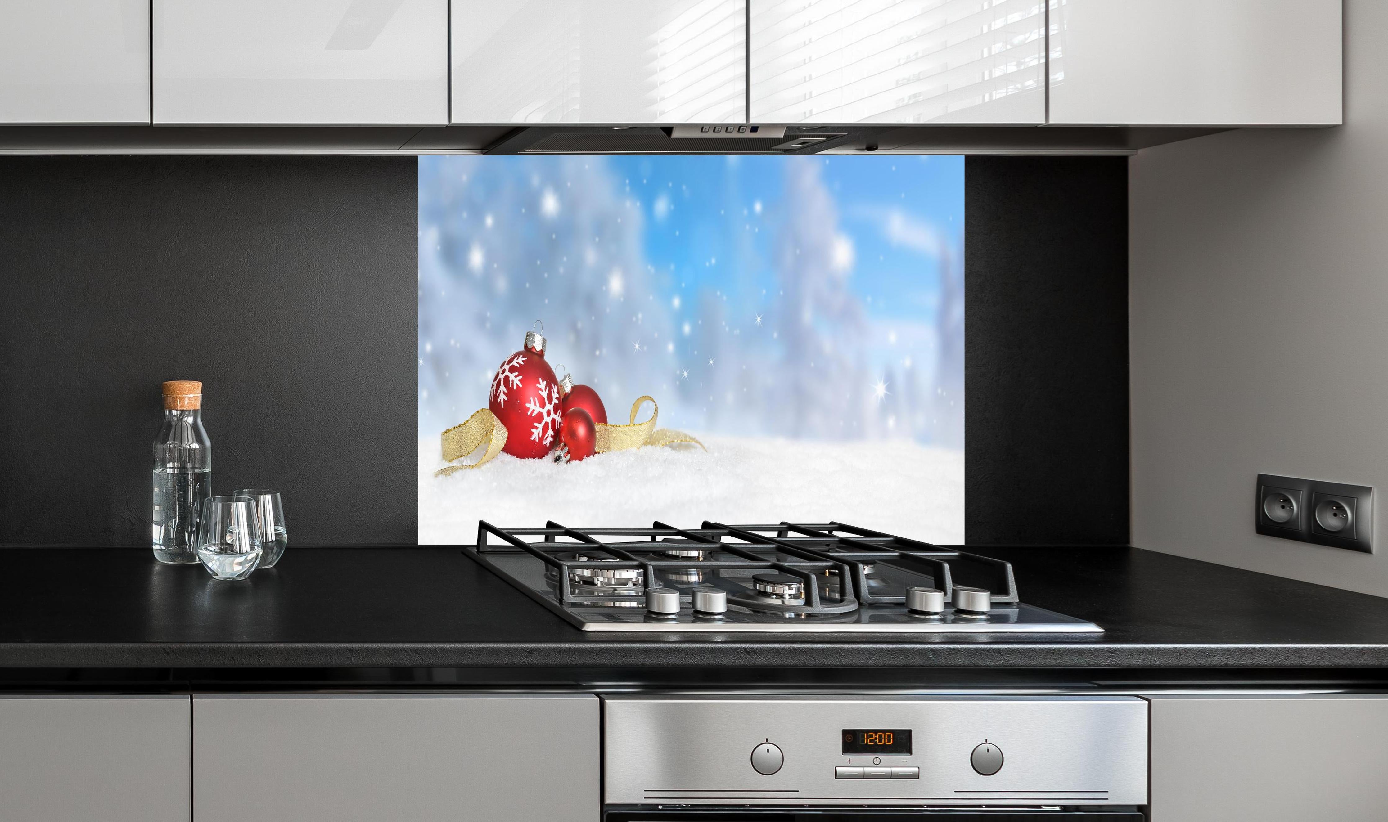 Spritzschutz - Weihnachtskugeln im Schnee hinter einem Cerankochfeld zwischen Holz-Kochutensilien