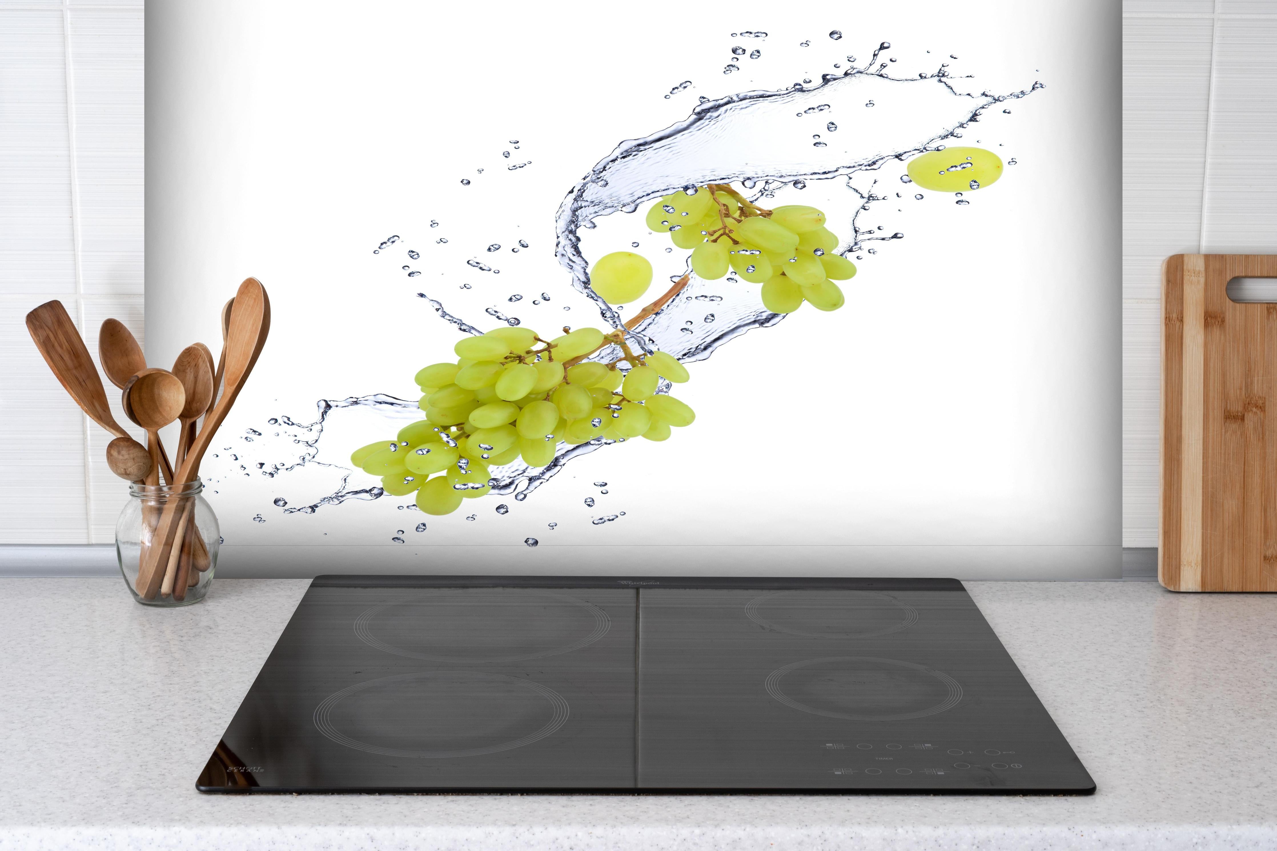 Spritzschutz - Weintraube im Wasserspritzer hinter einem Cerankochfeld zwischen Holz-Kochutensilien