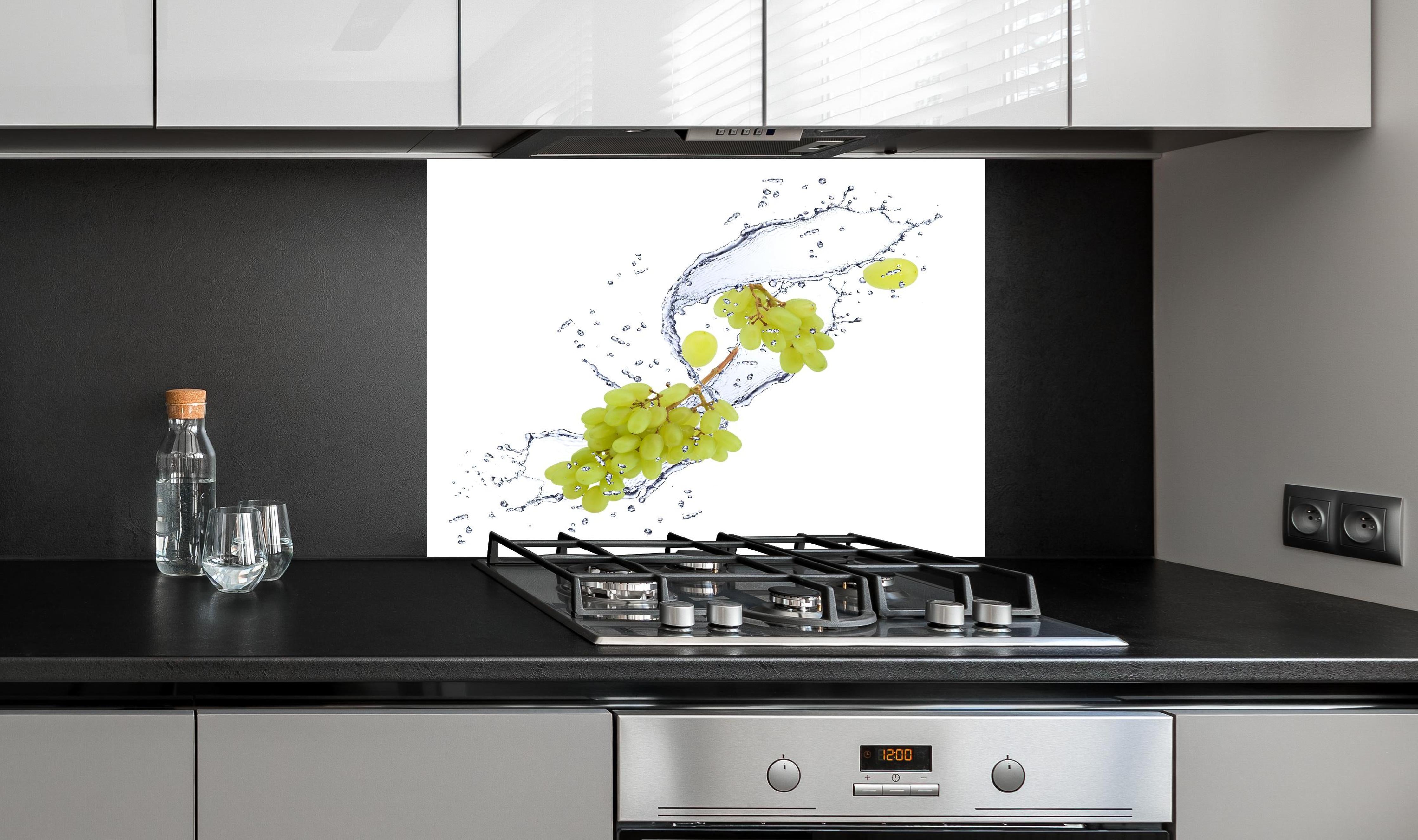 Spritzschutz - Weintraube im Wasserspritzer hinter einem Cerankochfeld zwischen Holz-Kochutensilien