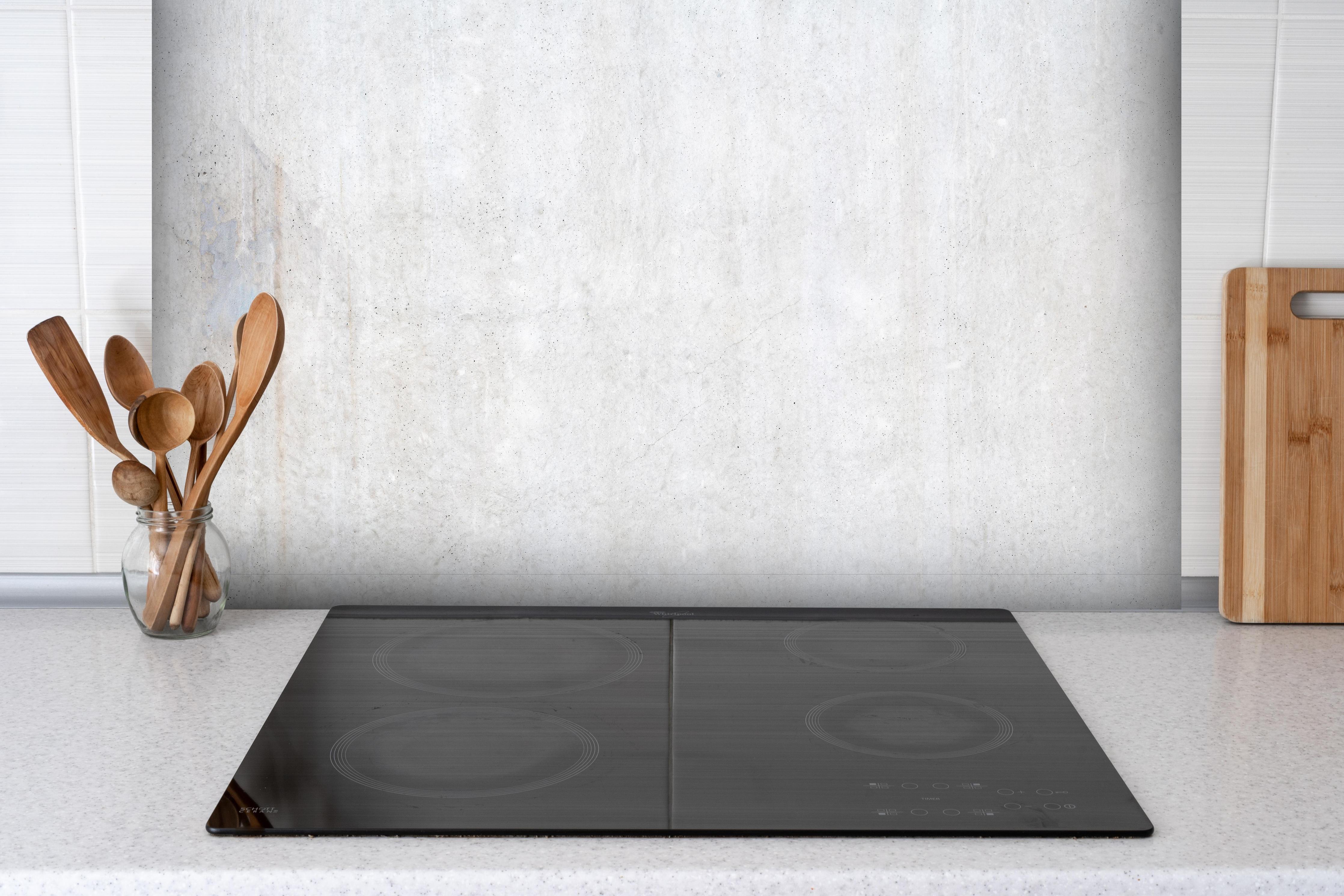 Spritzschutz - Weiß-bläuliche Betonwand hinter einem Cerankochfeld zwischen Holz-Kochutensilien