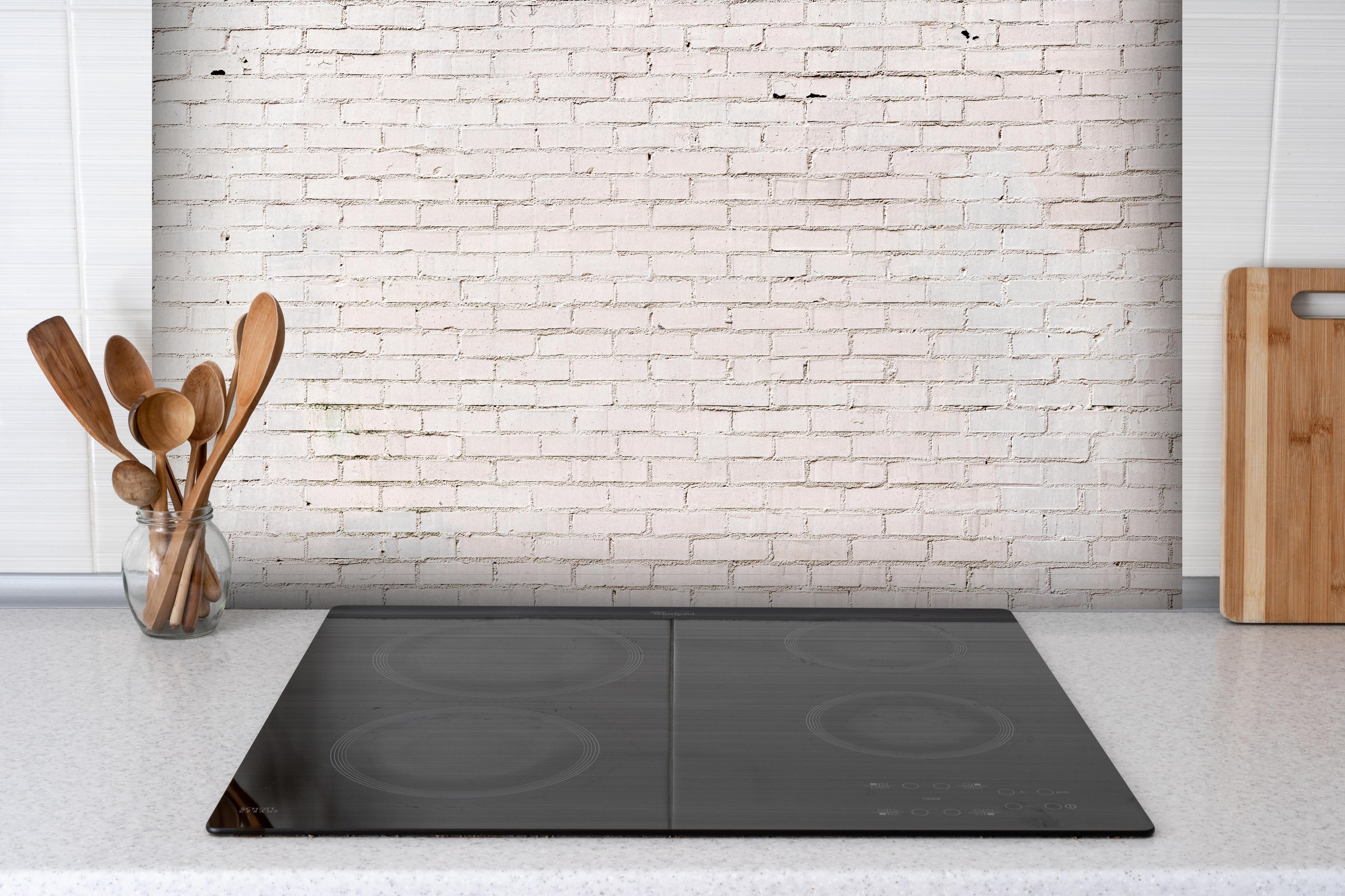 Spritzschutz - Weiß gestrichene Ziegelwand hinter einem Cerankochfeld zwischen Holz-Kochutensilien