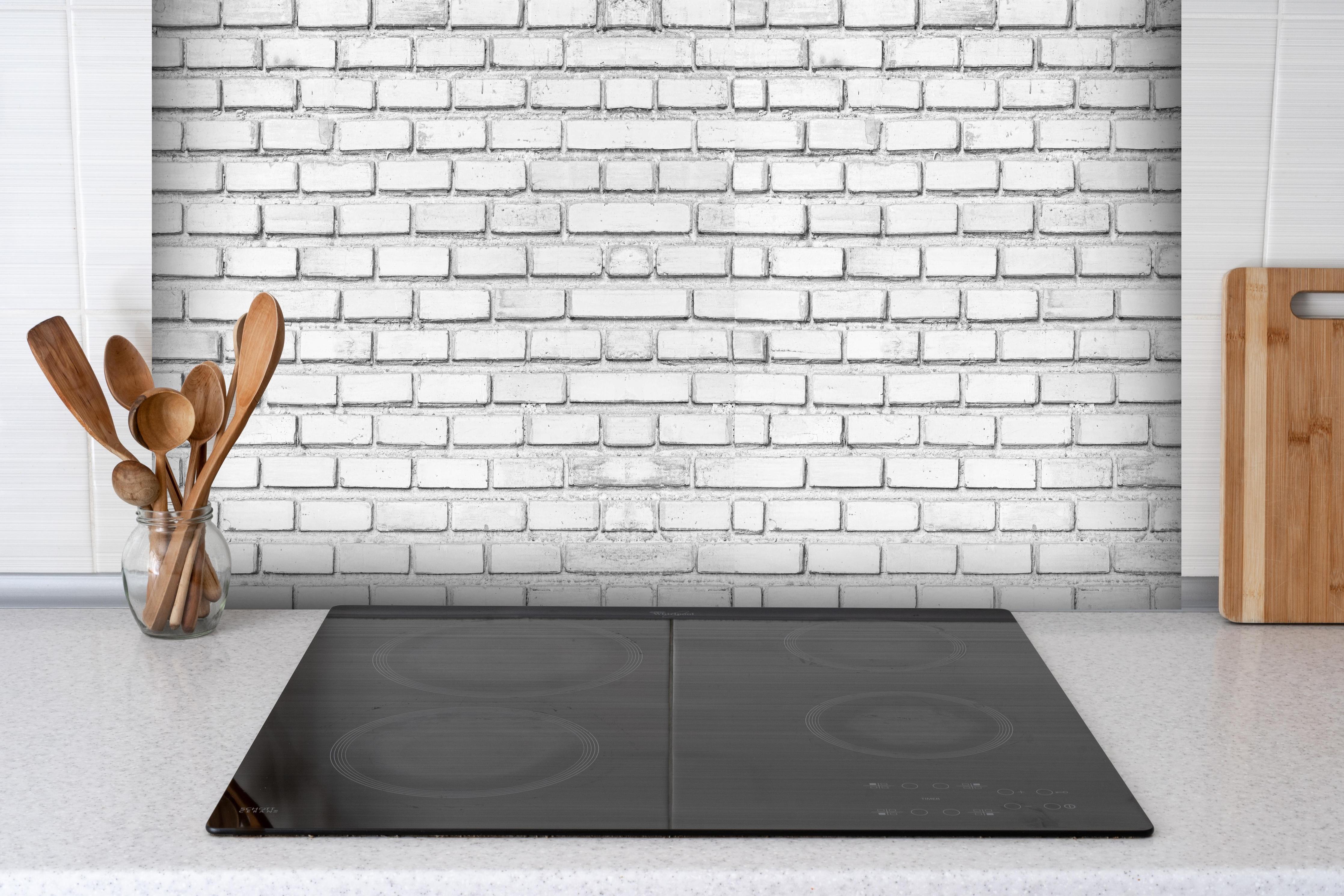 Spritzschutz - Weiße Backsteinmauer hinter einem Cerankochfeld zwischen Holz-Kochutensilien