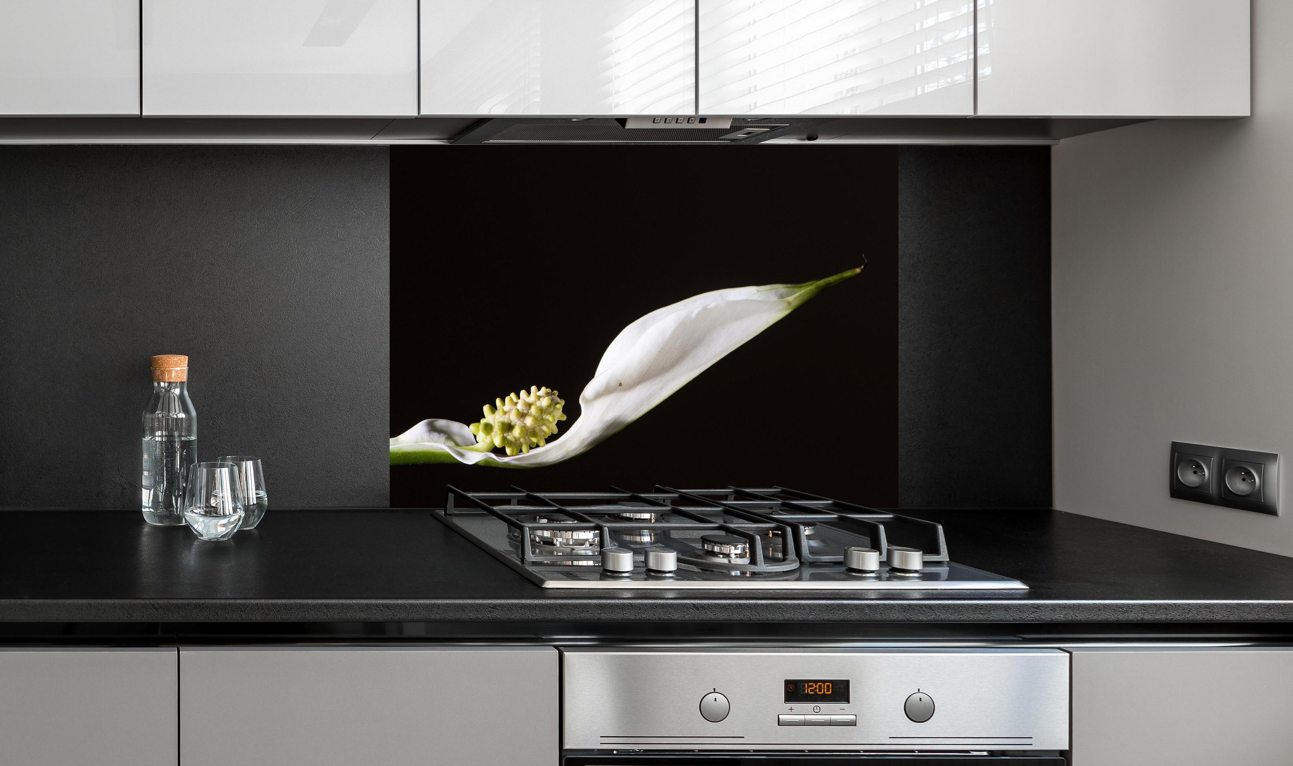 Spritzschutz - Weiße Blume auf schwarzem Hintergrund hinter einem Cerankochfeld zwischen Holz-Kochutensilien
