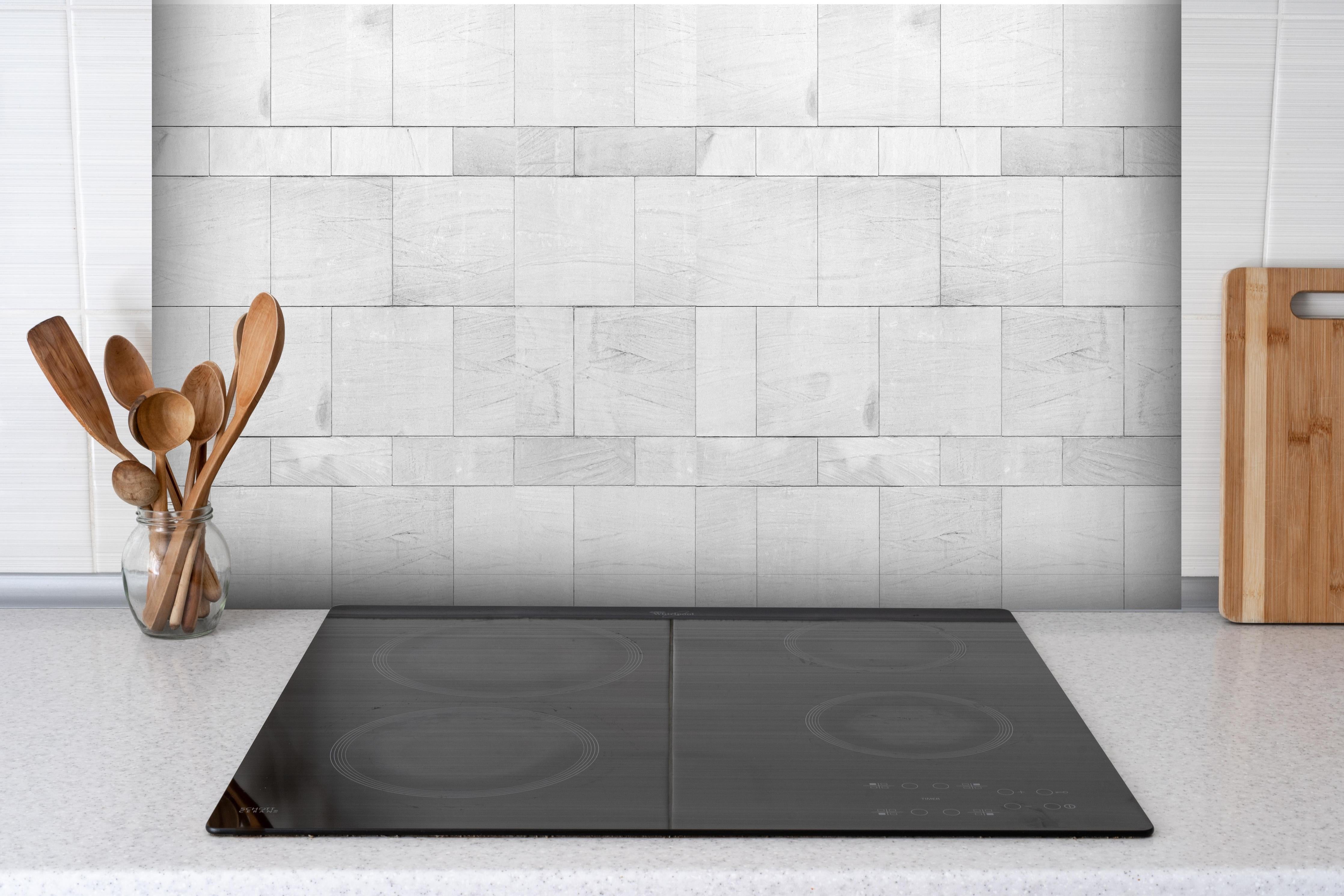 Spritzschutz - Weiße Granit Fliesen hinter einem Cerankochfeld zwischen Holz-Kochutensilien