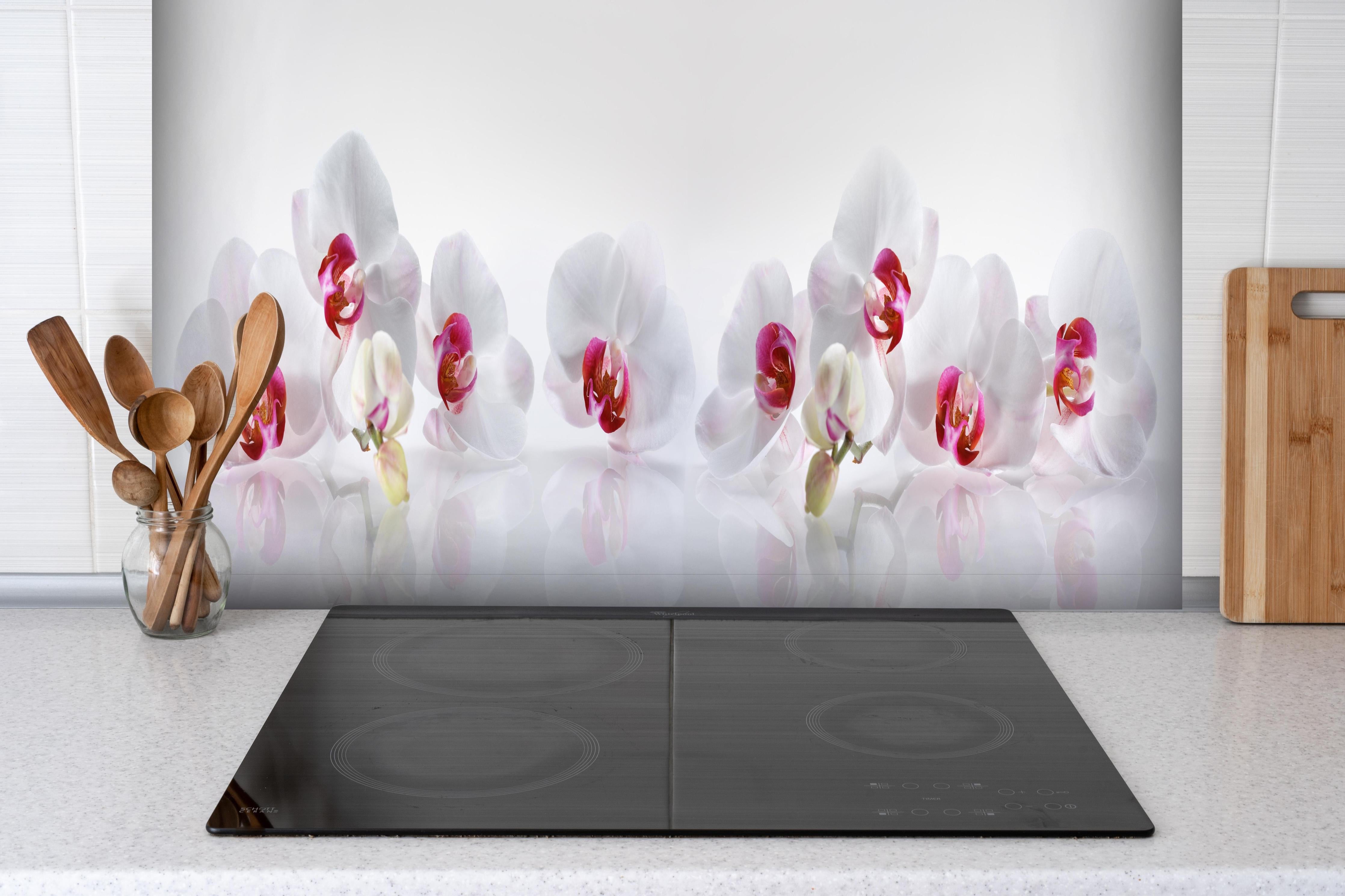 Spritzschutz - Weiße Orchideen hinter einem Cerankochfeld zwischen Holz-Kochutensilien