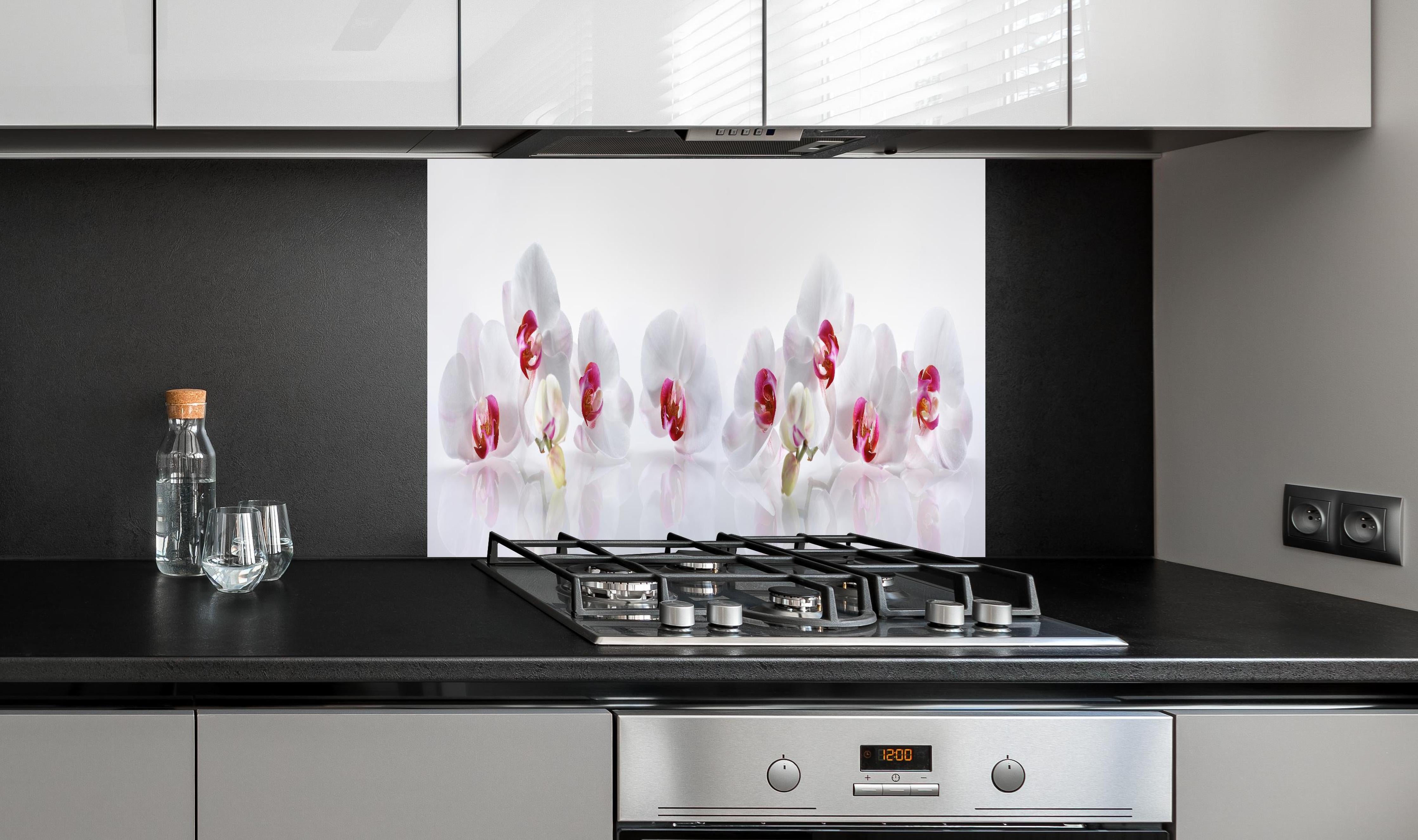 Spritzschutz - Weiße Orchideen hinter einem Cerankochfeld zwischen Holz-Kochutensilien