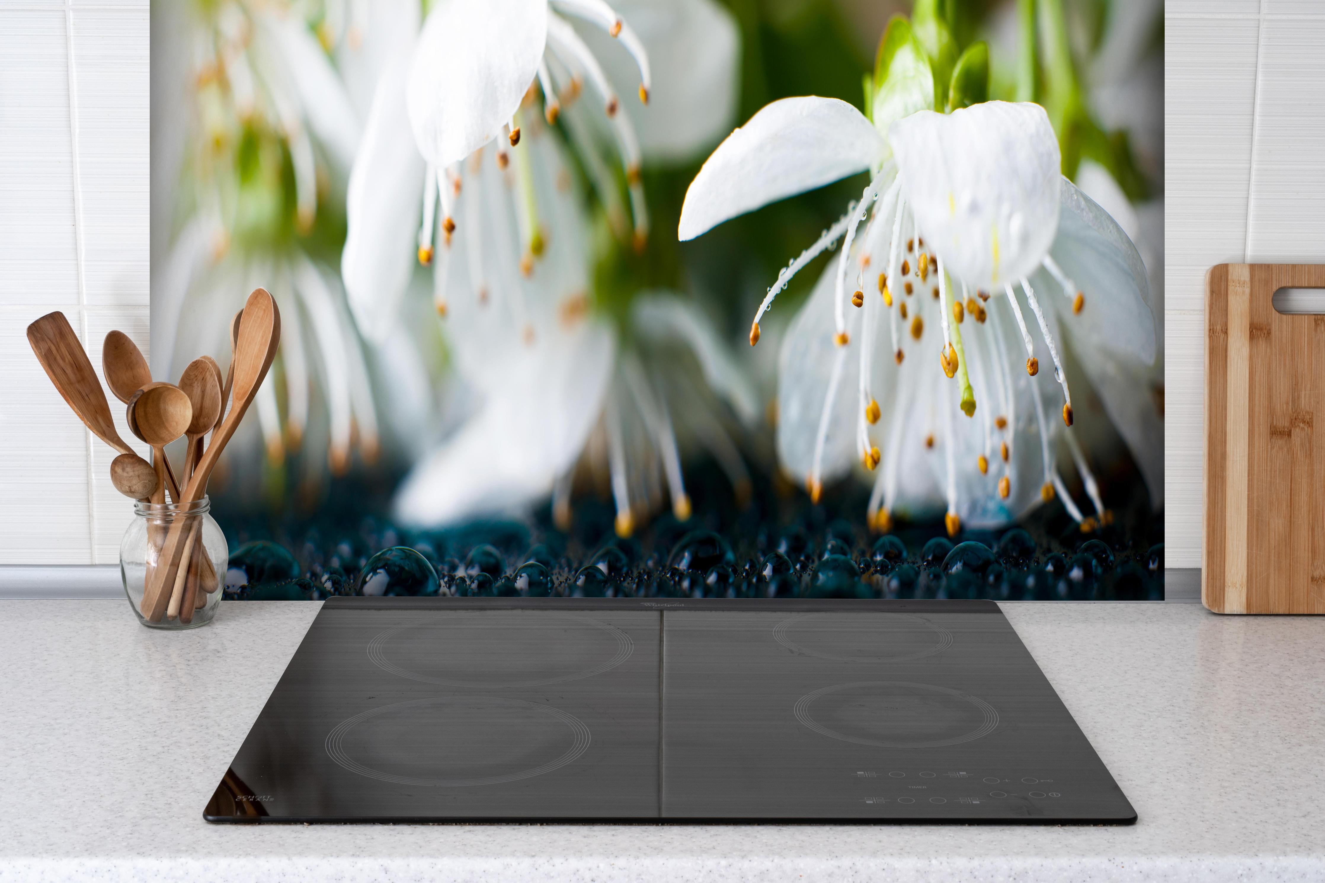 Spritzschutz - Weiße blühende Frühlingsblumen hinter einem Cerankochfeld zwischen Holz-Kochutensilien