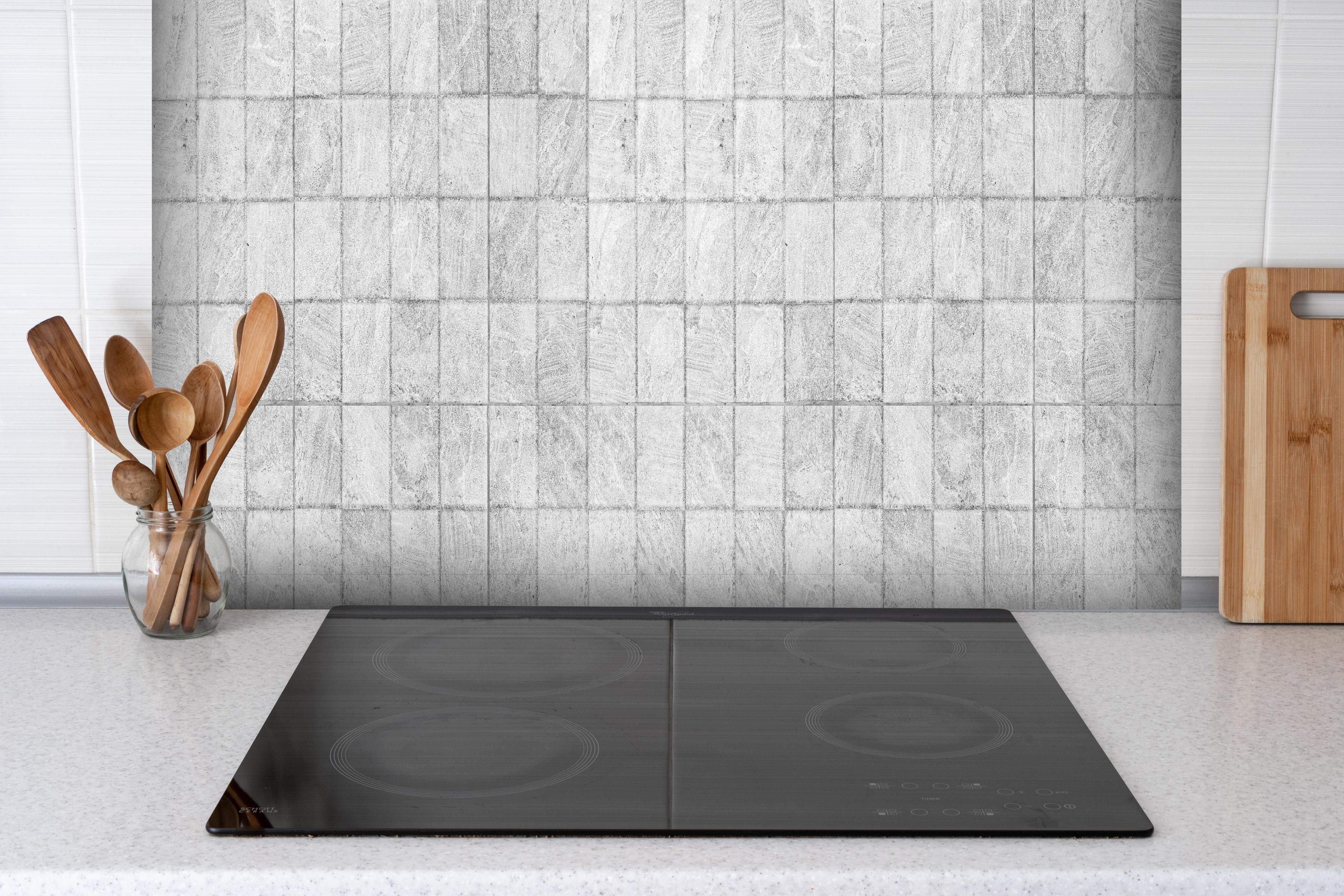 Spritzschutz - Weiße quadratische Stein Fliesen hinter einem Cerankochfeld zwischen Holz-Kochutensilien