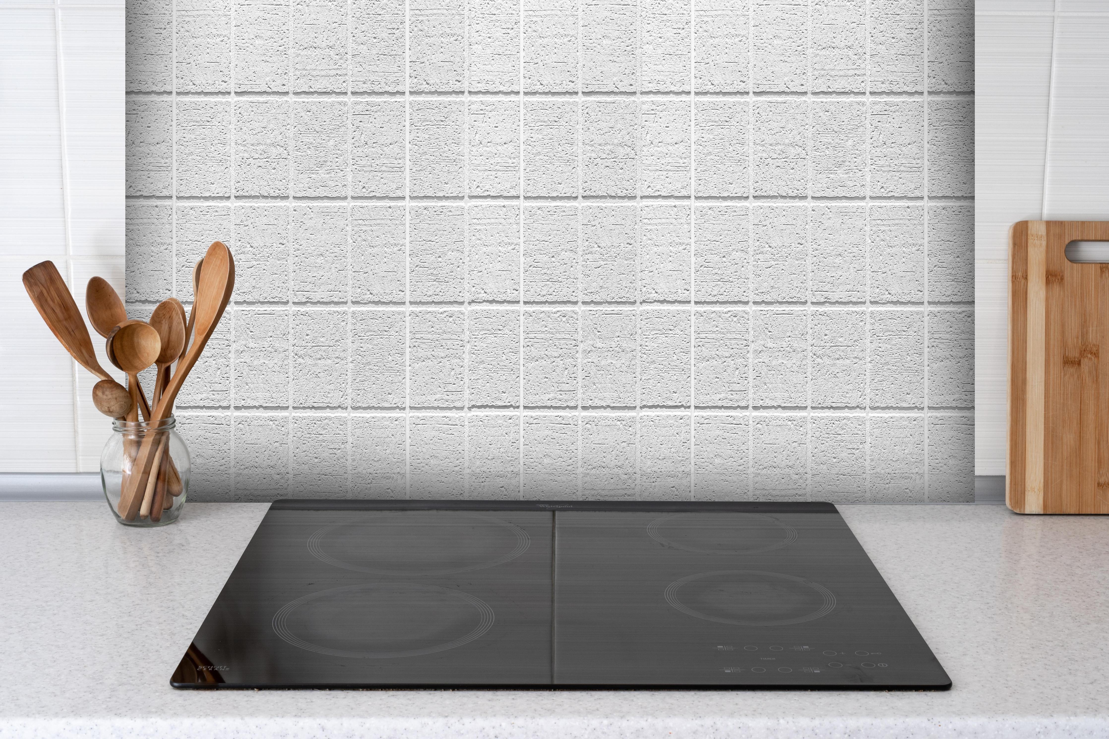 Spritzschutz - Weiße quadratische Steintextur hinter einem Cerankochfeld zwischen Holz-Kochutensilien