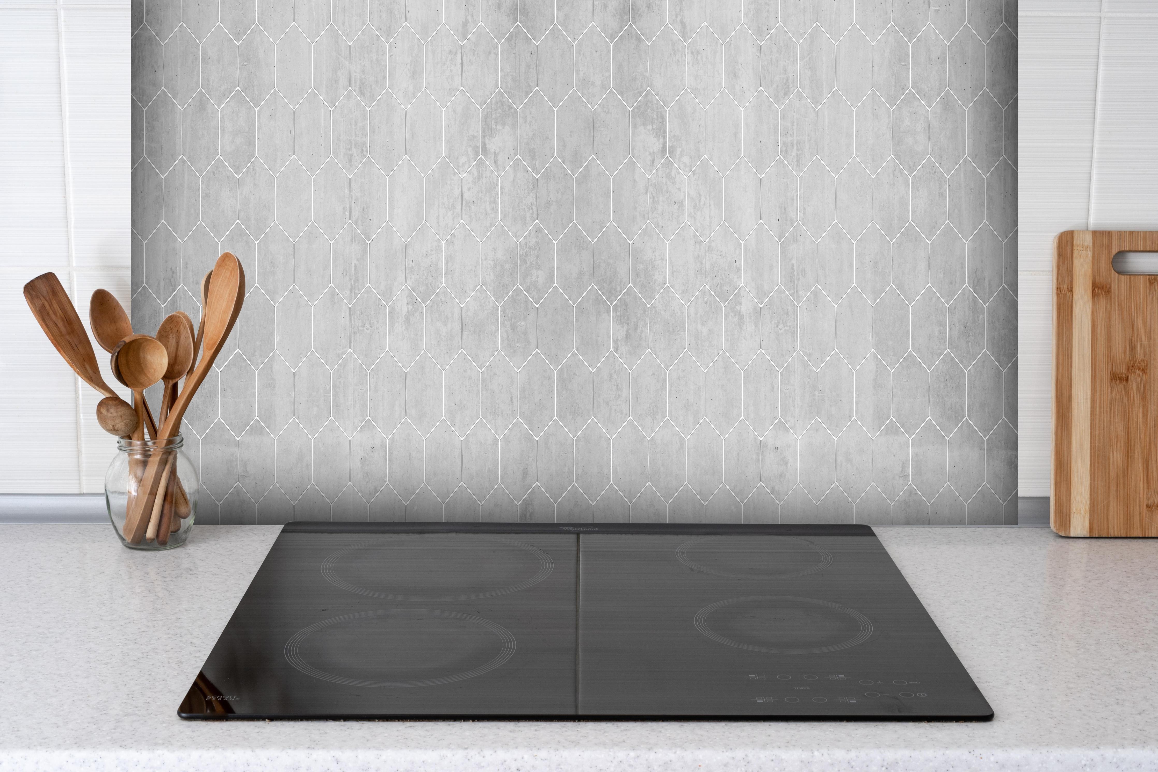 Spritzschutz - Weiße sechseckige Mustern auf Grauen Hintergrund hinter einem Cerankochfeld zwischen Holz-Kochutensilien