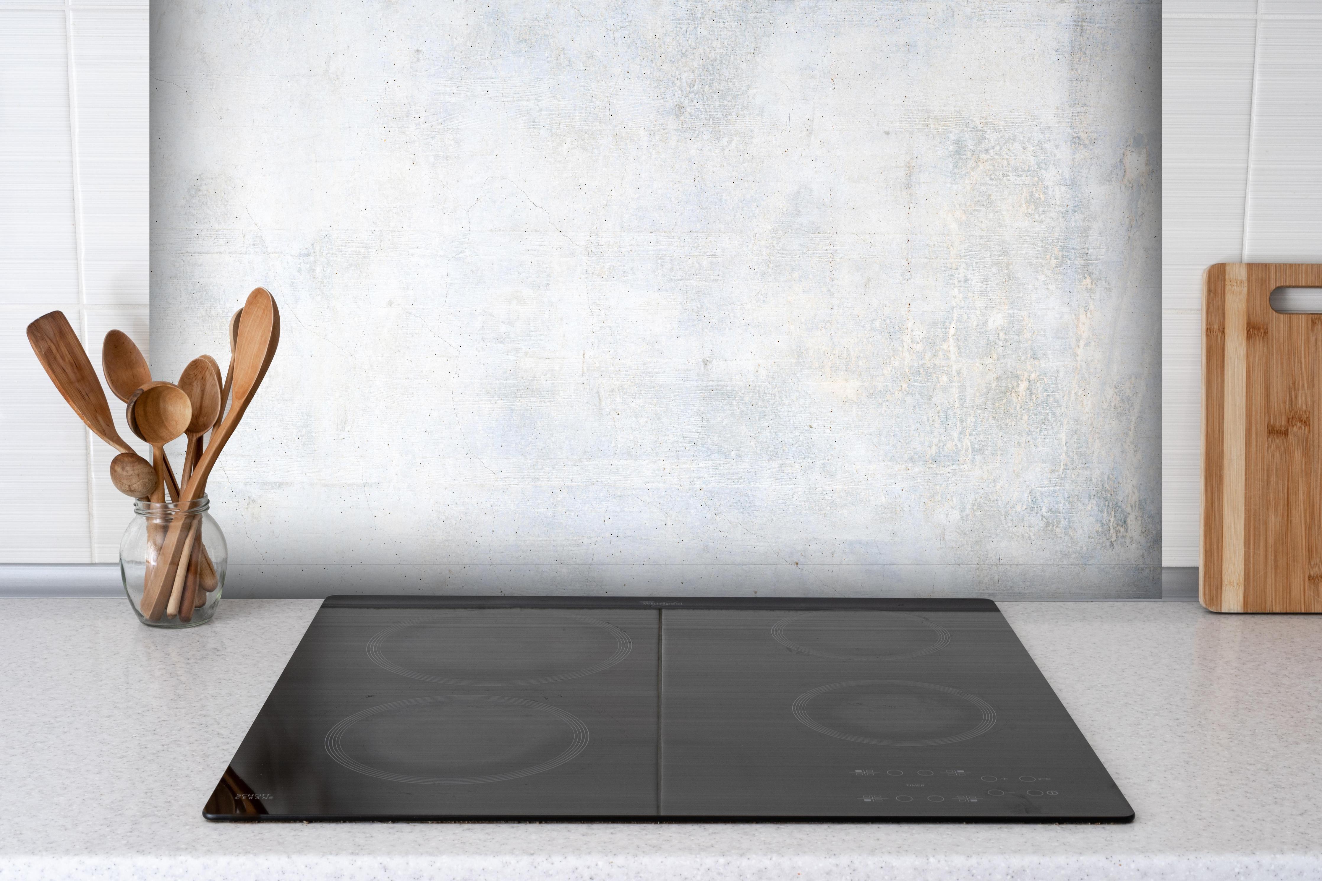 Spritzschutz - Weiße verwitterte Betonwand hinter einem Cerankochfeld zwischen Holz-Kochutensilien