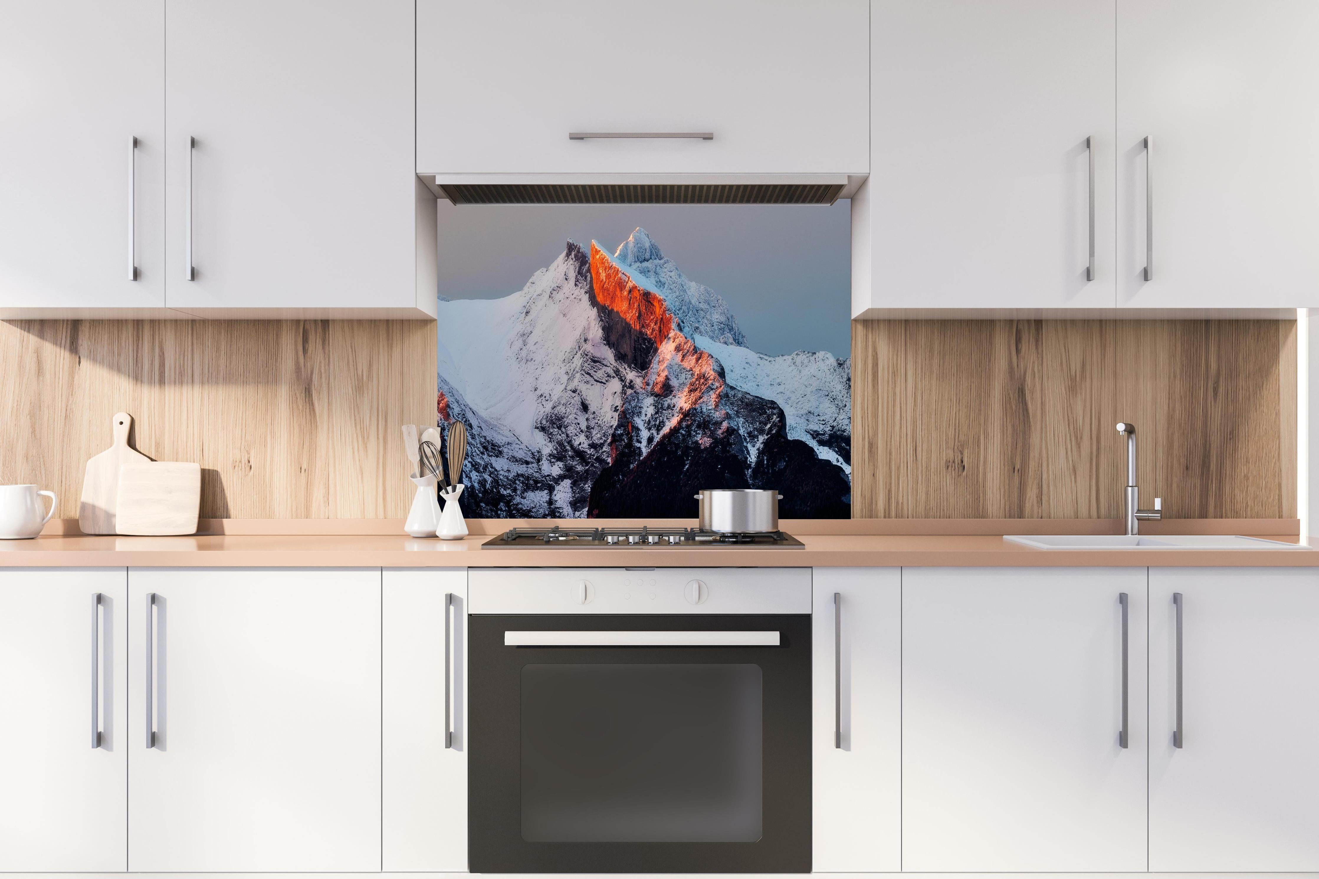 Spritzschutz - Winterlicher Sonnenaufgang über schneebedeckten Gipfeln hinter einem Cerankochfeld zwischen Holz-Kochutensilien