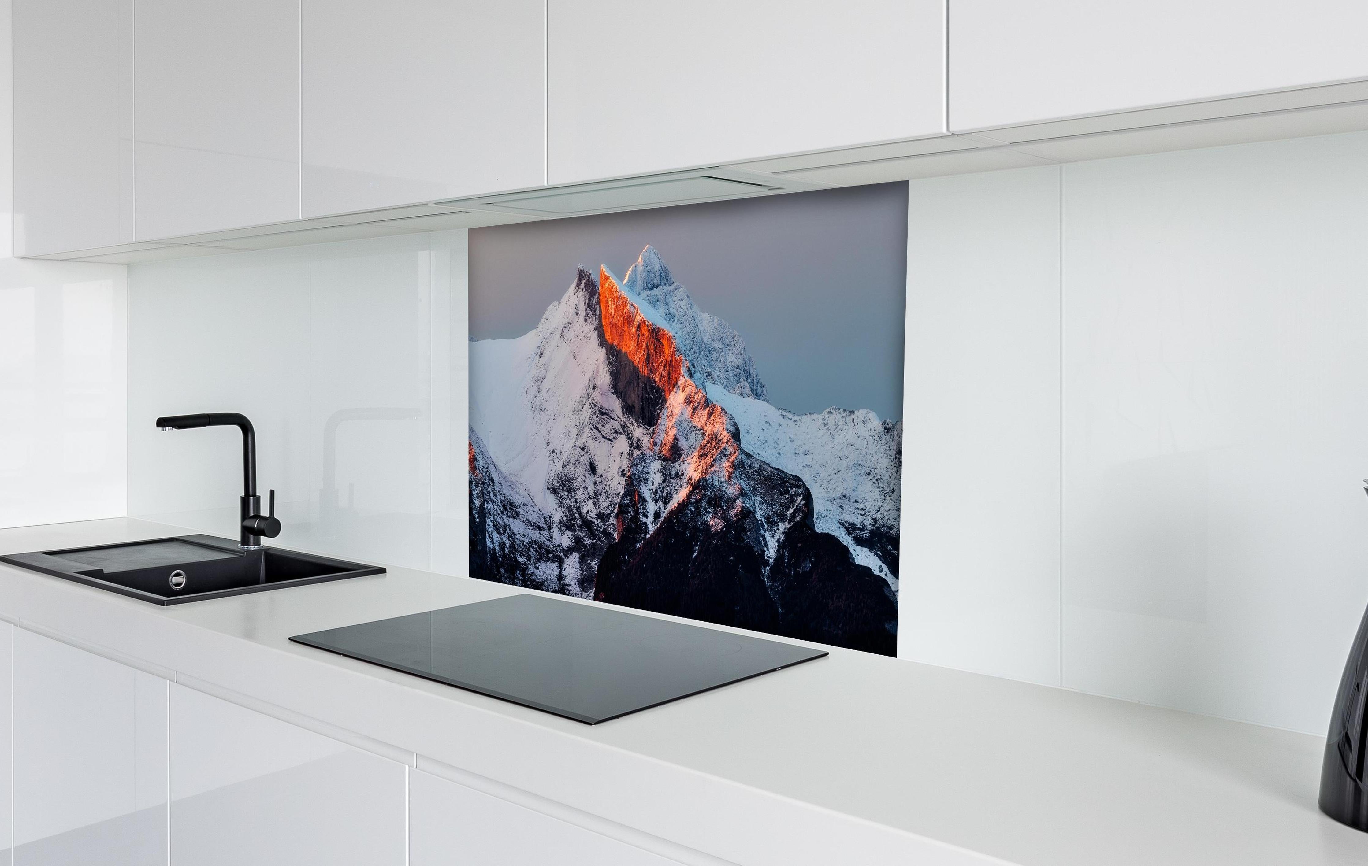 Spritzschutz - Winterlicher Sonnenaufgang über schneebedeckten Gipfeln hinter einem Cerankochfeld zwischen Holz-Kochutensilien