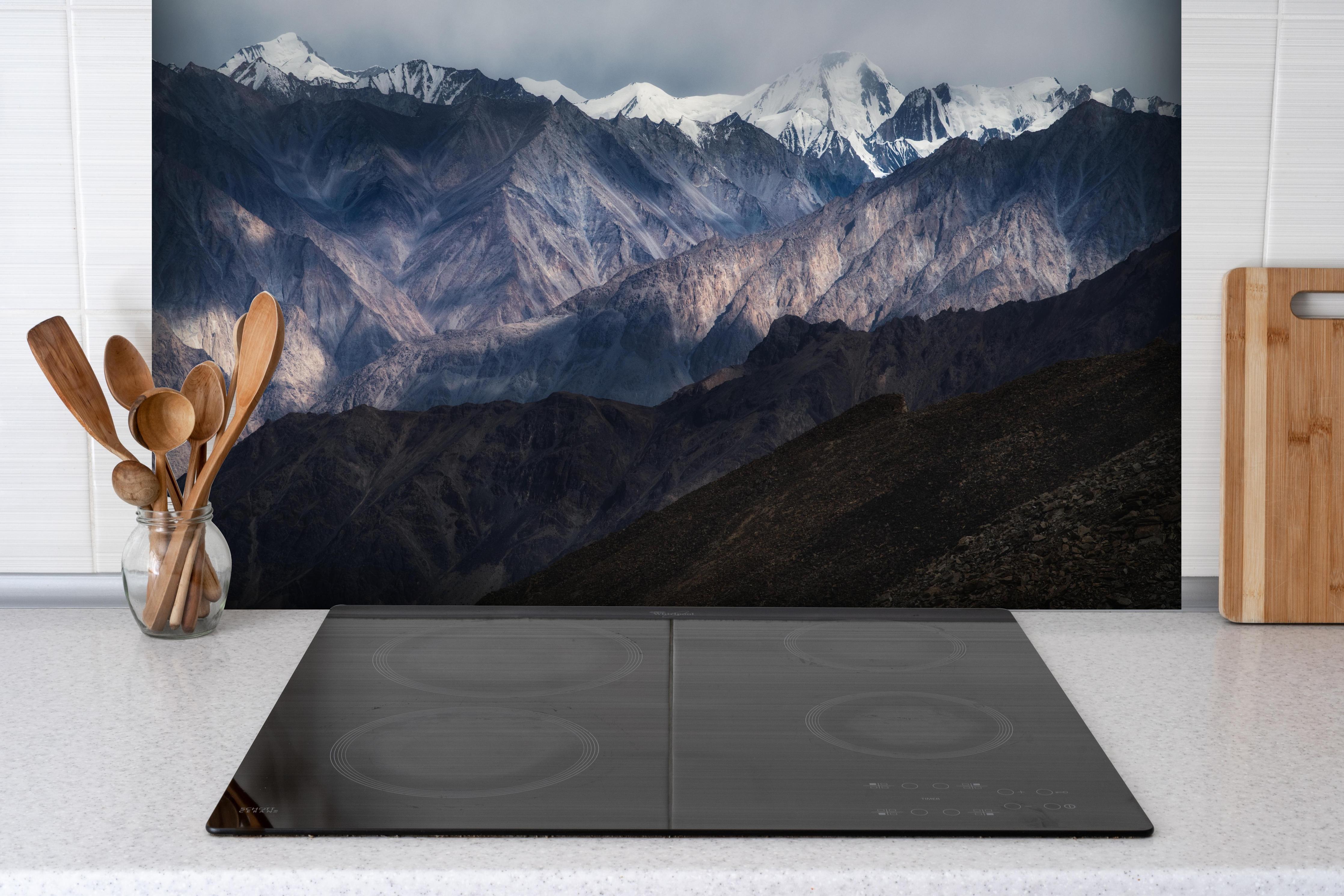 Spritzschutz - Winterliches Bergpanorama mit Schnee und Felsen hinter einem Cerankochfeld zwischen Holz-Kochutensilien