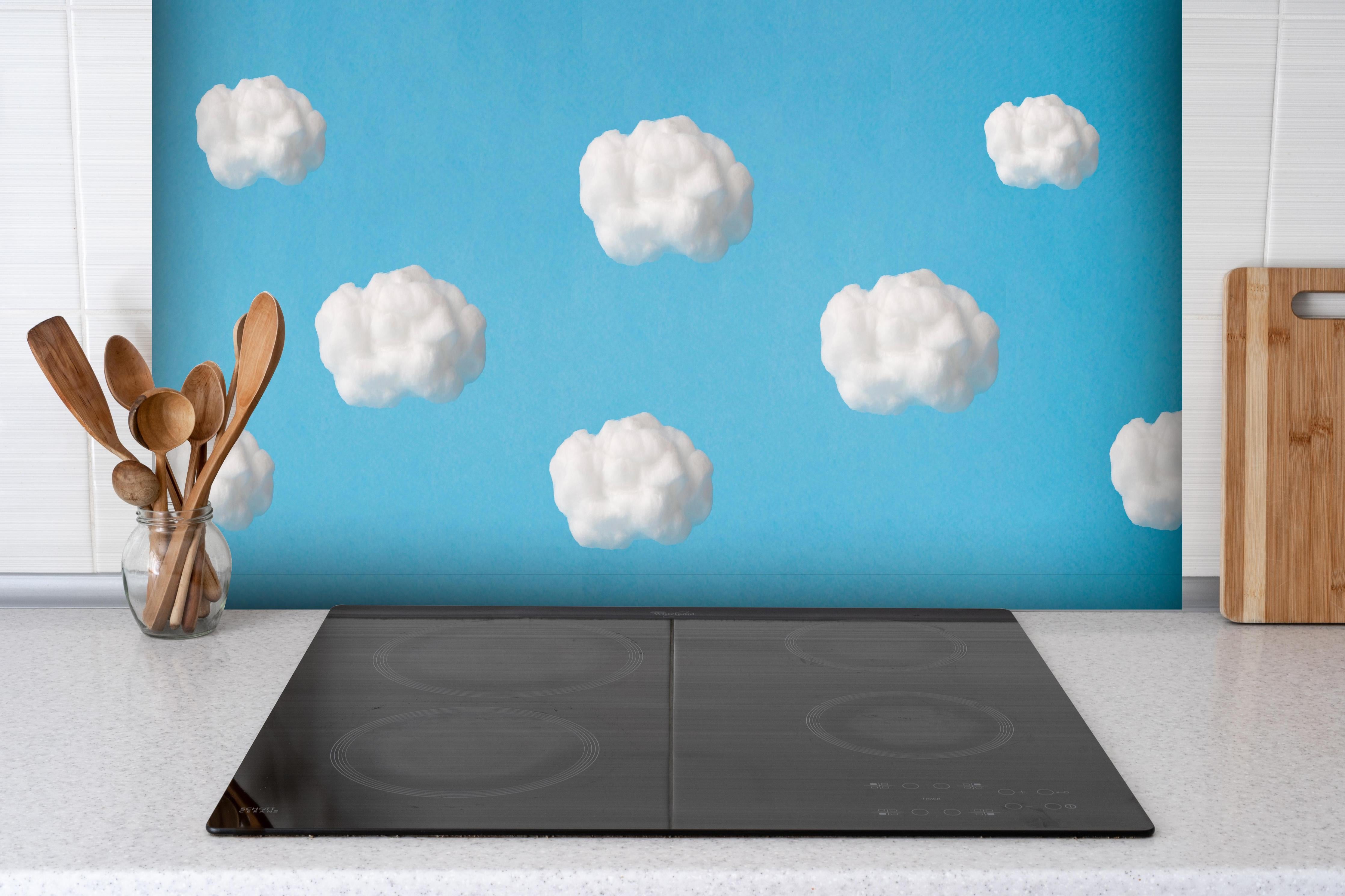Spritzschutz - Wolke aus Watte auf himmelblauem Hintergrund hinter einem Cerankochfeld zwischen Holz-Kochutensilien