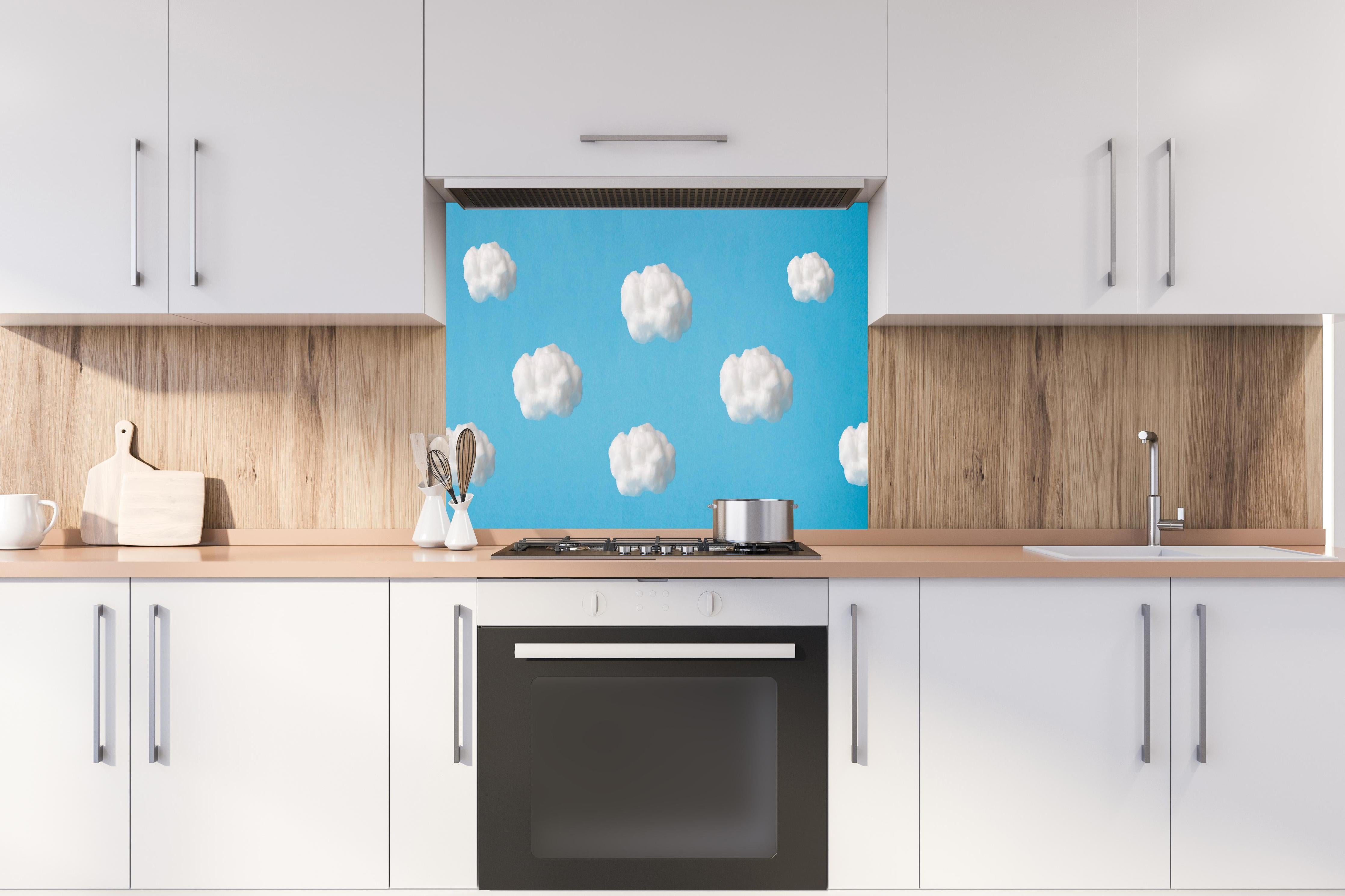Spritzschutz - Wolke aus Watte auf himmelblauem Hintergrund hinter einem Cerankochfeld zwischen Holz-Kochutensilien