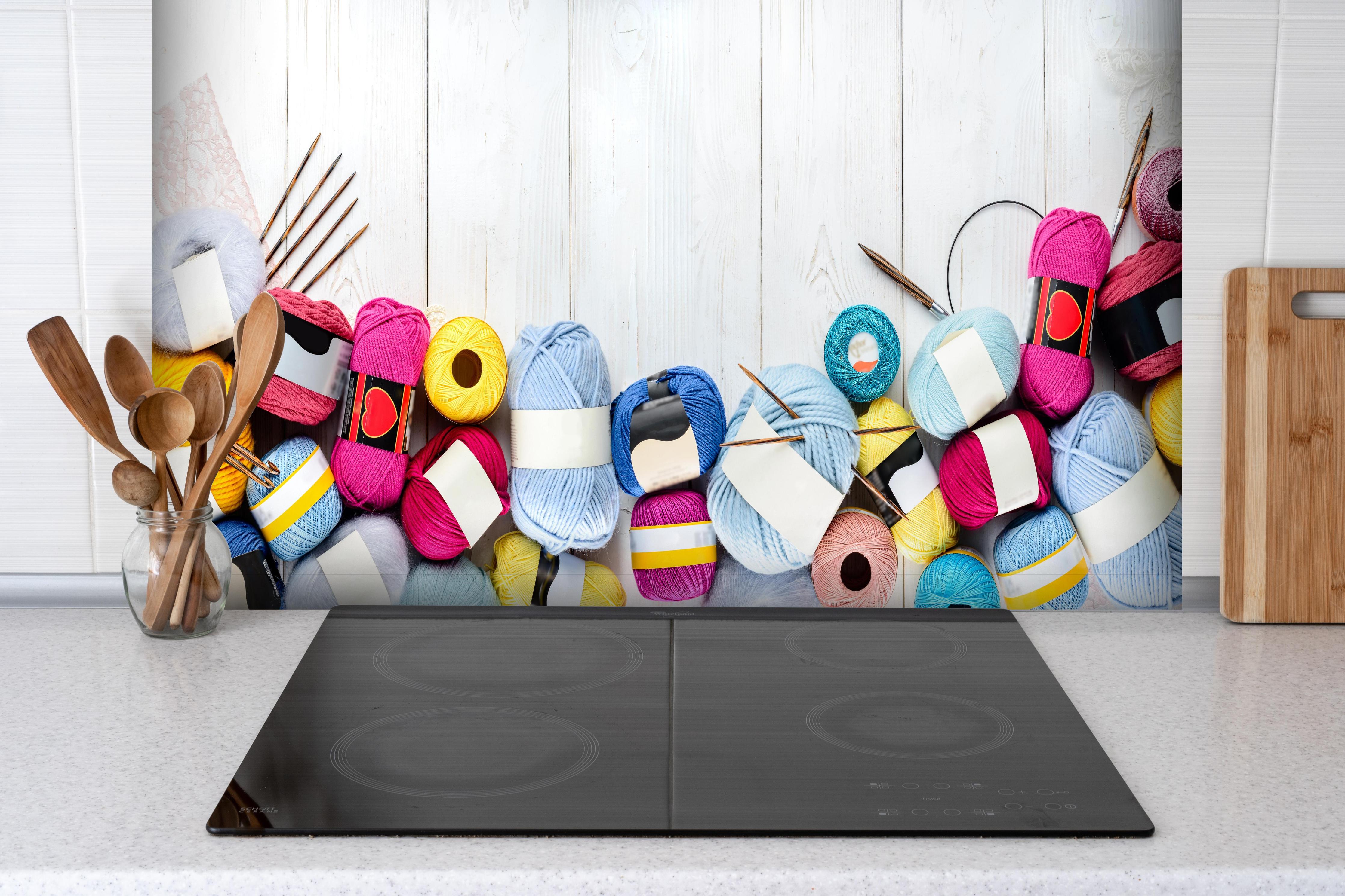 Spritzschutz - Wolle und Stricknadeln auf Holzhintergrund hinter einem Cerankochfeld zwischen Holz-Kochutensilien