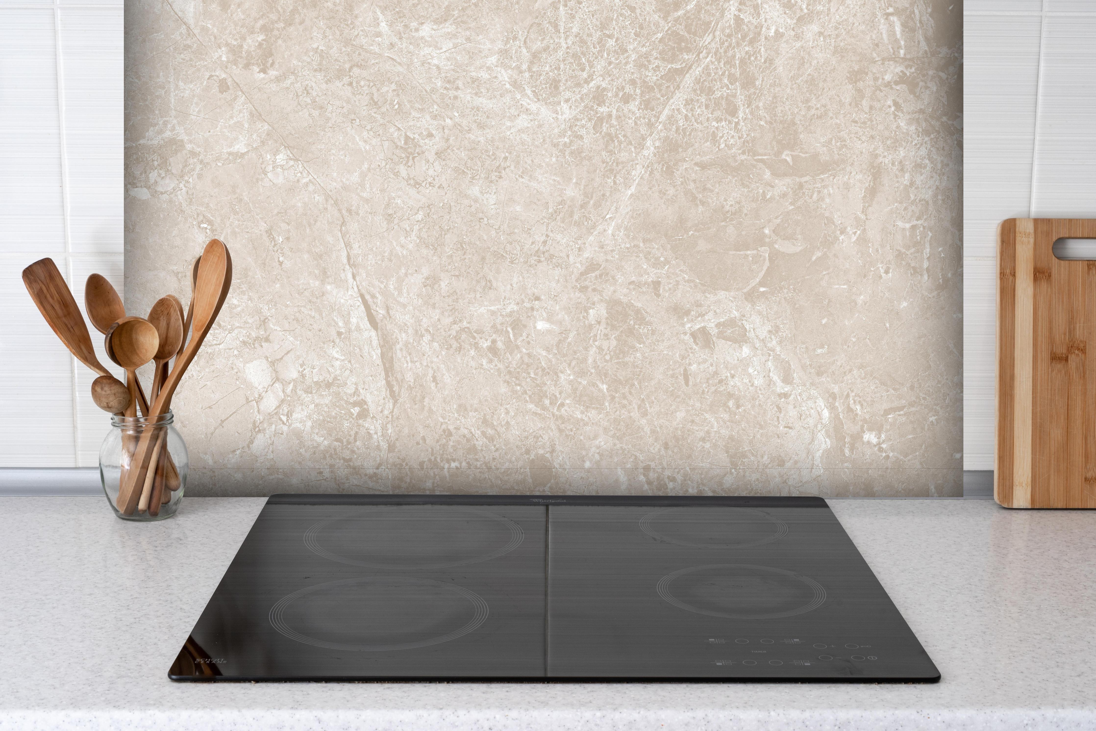 Spritzschutz - beiger Naturmarmor hinter einem Cerankochfeld zwischen Holz-Kochutensilien