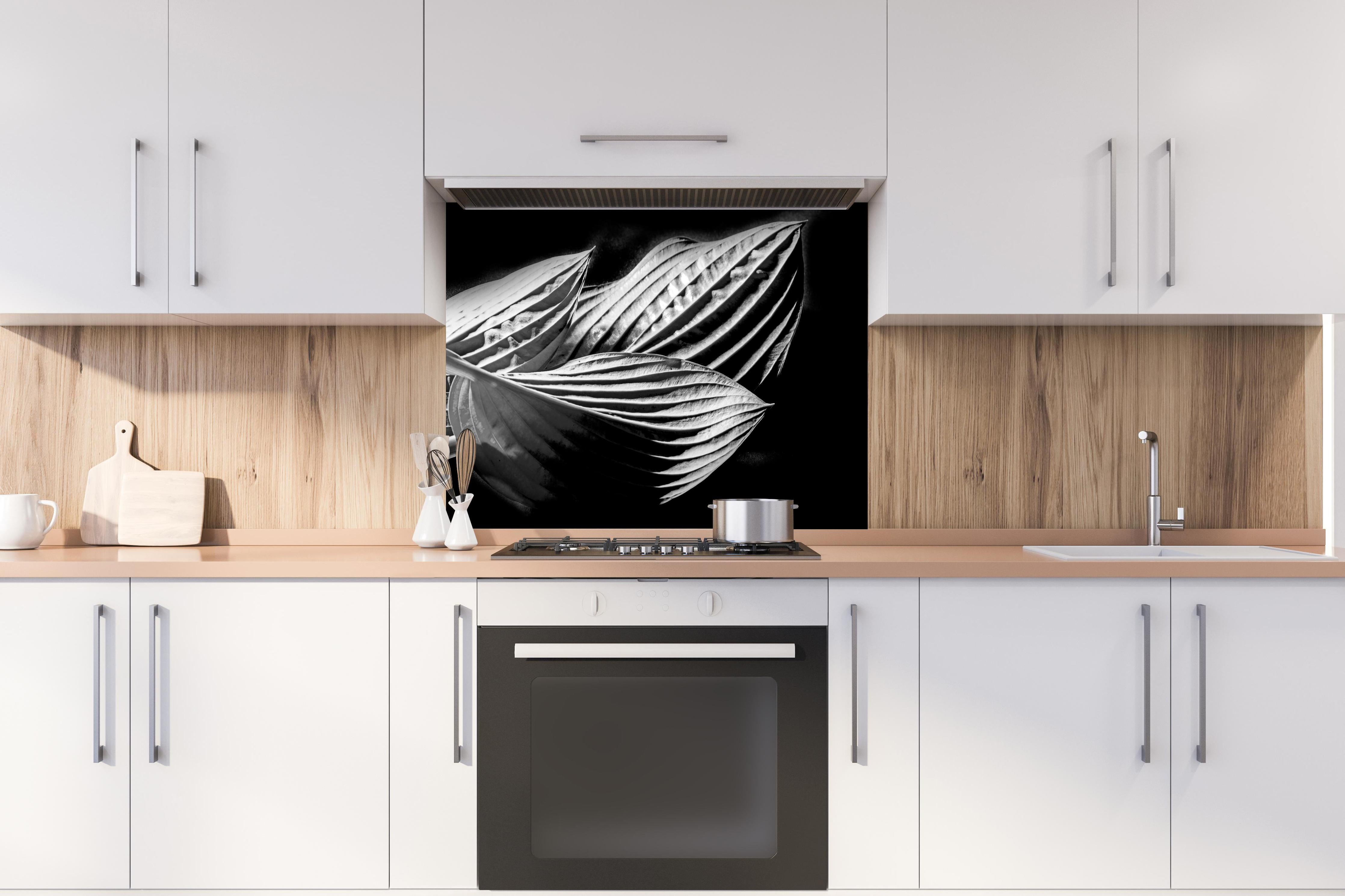 Spritzschutz - drei Blätter auf dunklem Hintergrund hinter einem Cerankochfeld zwischen Holz-Kochutensilien