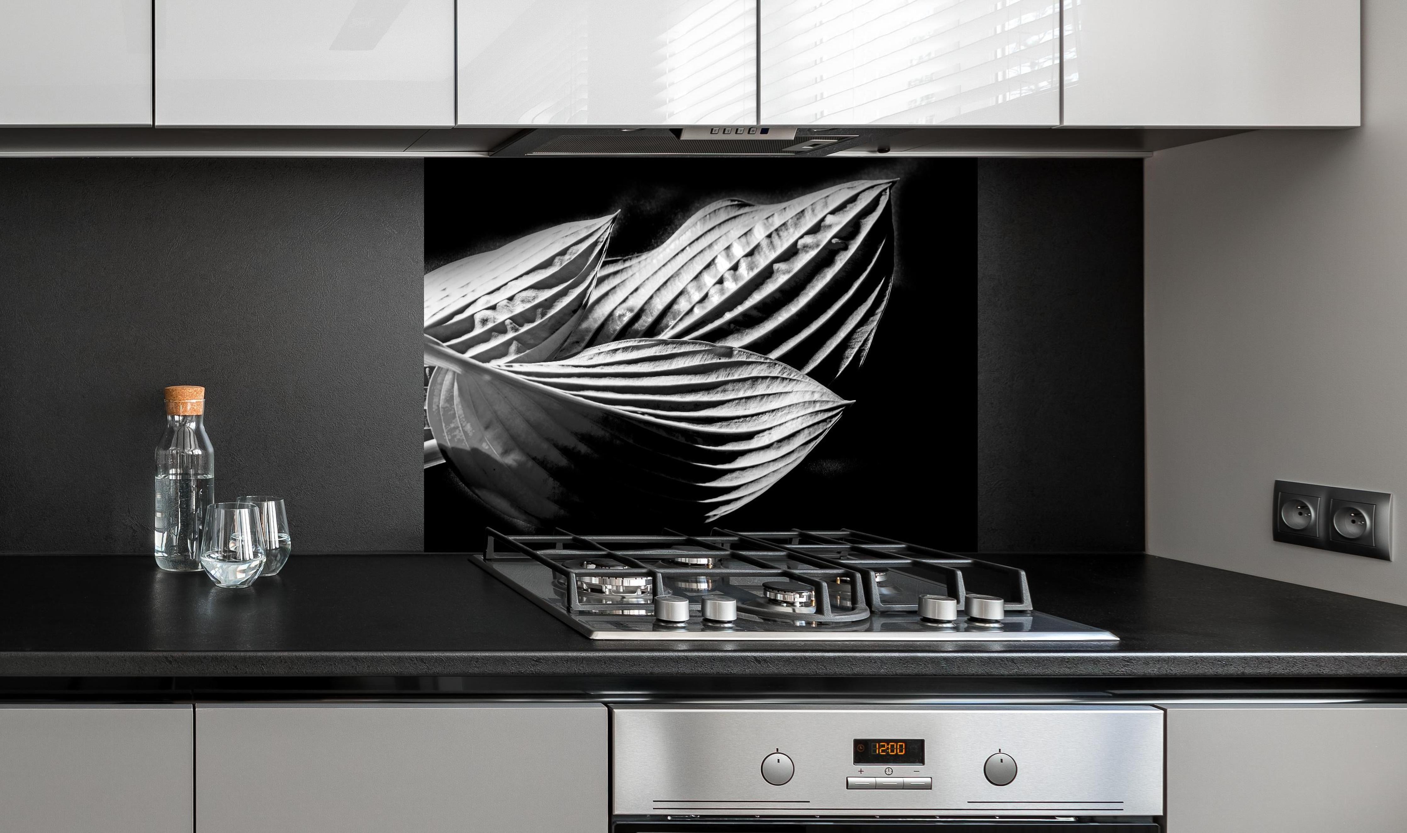 Spritzschutz - drei Blätter auf dunklem Hintergrund hinter einem Cerankochfeld zwischen Holz-Kochutensilien