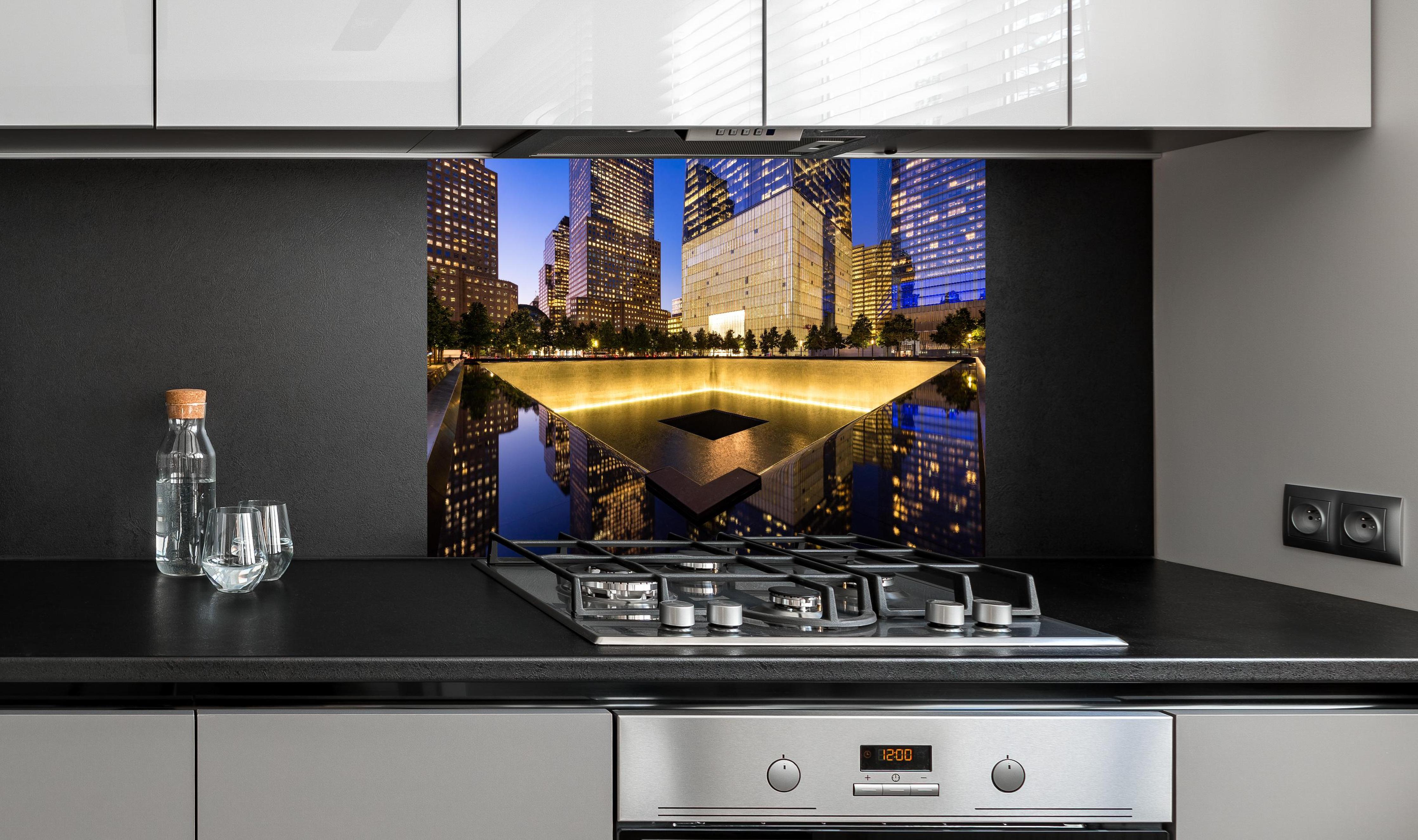 Spritzschutz - nächtlich Beleuchtetes World Trade Center Site hinter einem Cerankochfeld zwischen Holz-Kochutensilien