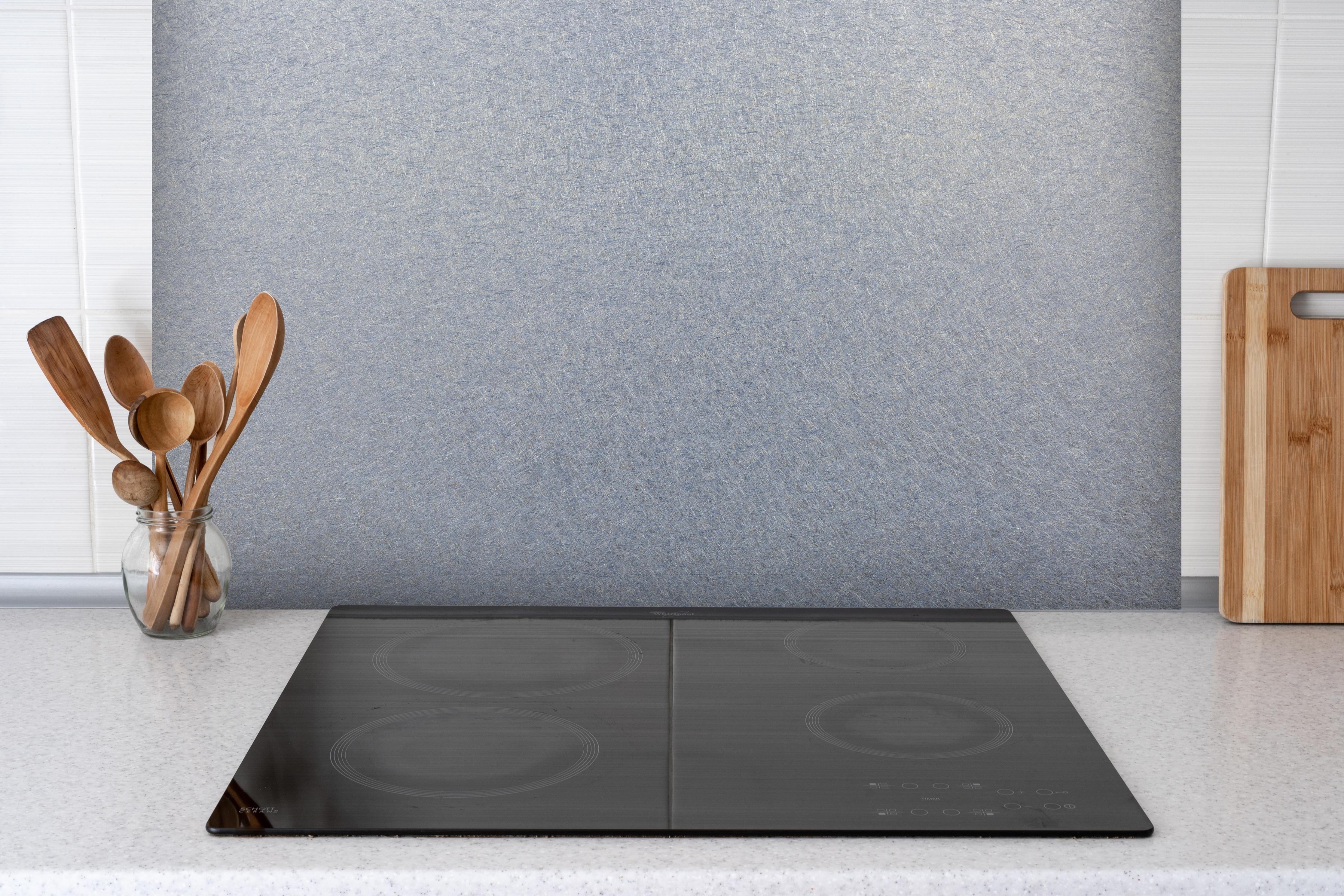 Spritzschutz - Spritzschutz - Zerkratzte metallische Oberfläche hinter einem Cerankochfeld zwischen Holz-Kochutensilien