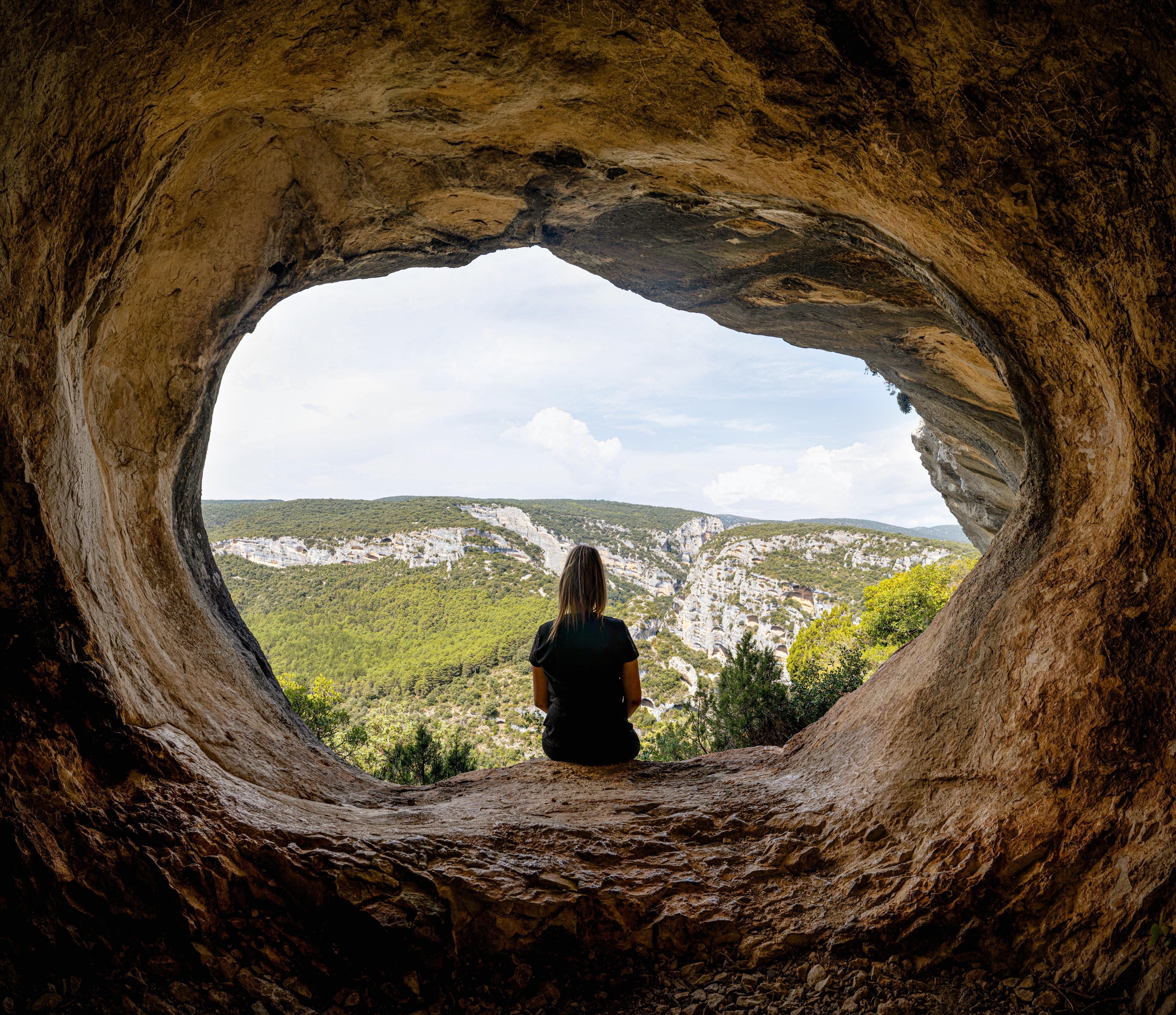 Duschrückwand-Frau sitzend in Berghöhle mit Blick auf Landschaft