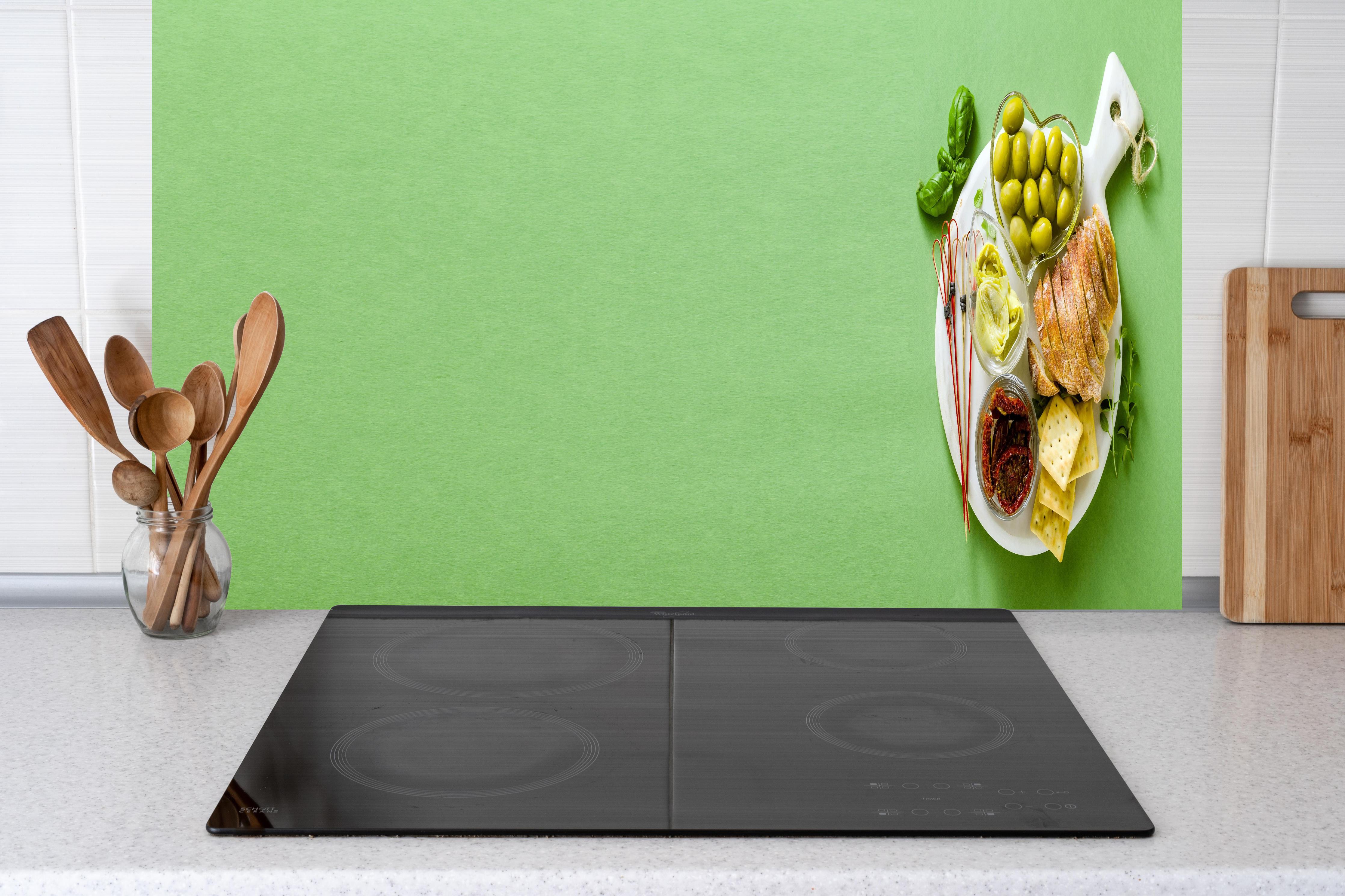 Küche - Grüne Küchenrückwand mit Oliven hinter Cerankochfeld und Holz-Kochutensilien