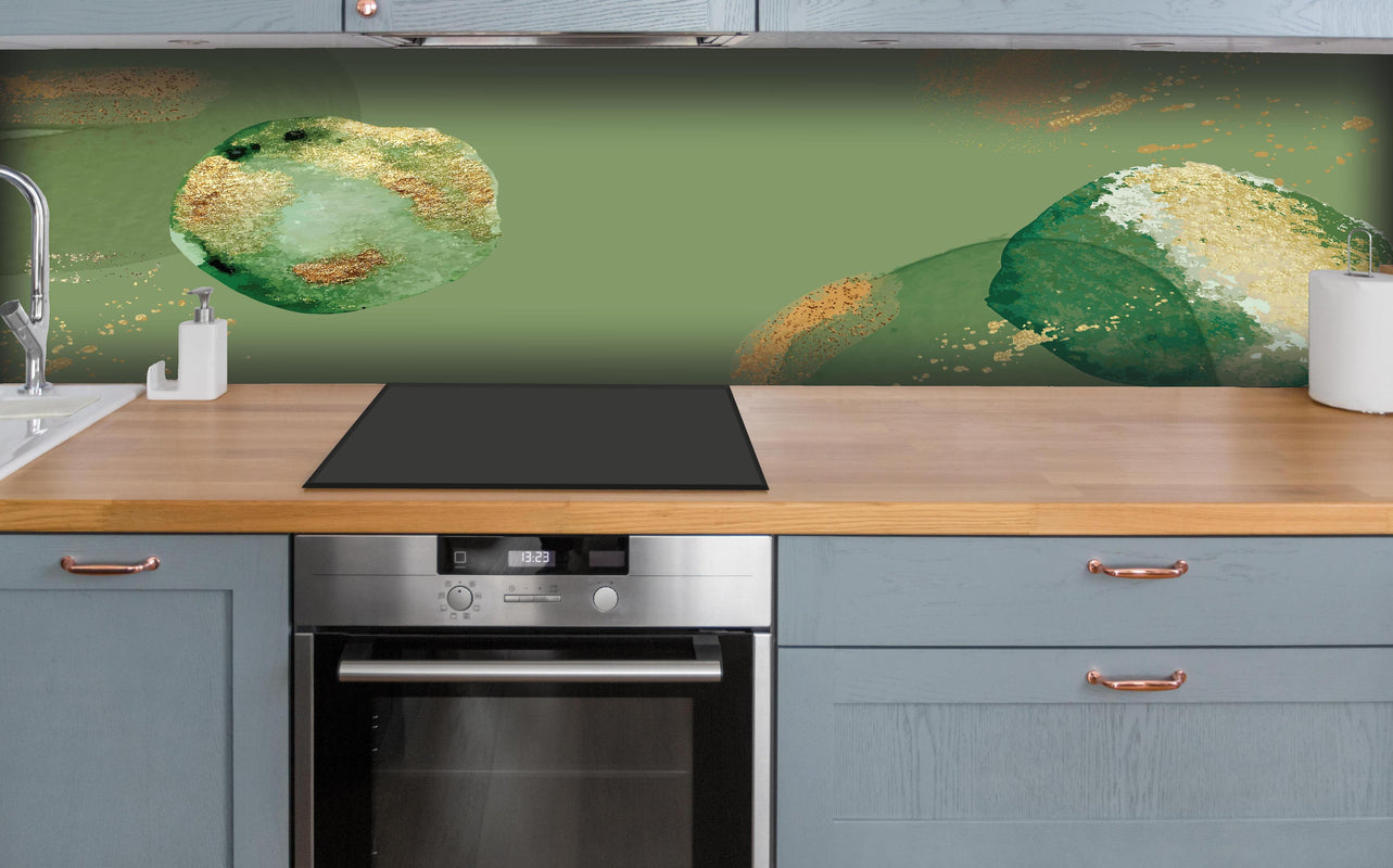 Küche - Abstraktes Design mit Grün und Goldtönen hinter weißen Hochglanz-Küchenregalen und schwarzem Wasserhahn