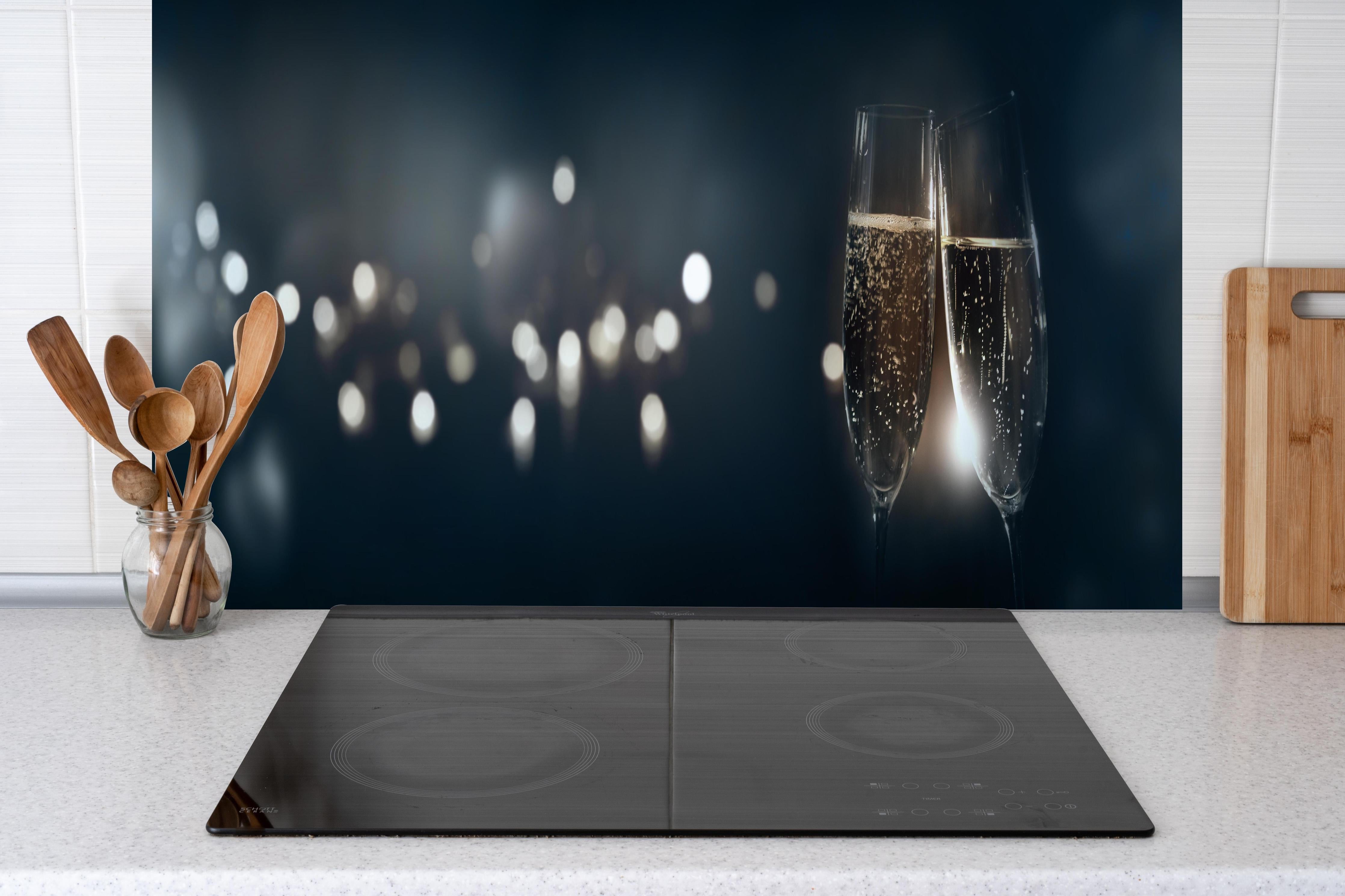 Küche - Anstoßen mit funkelndem Champagner hinter weißen Hochglanz-Küchenregalen und schwarzem Wasserhahn